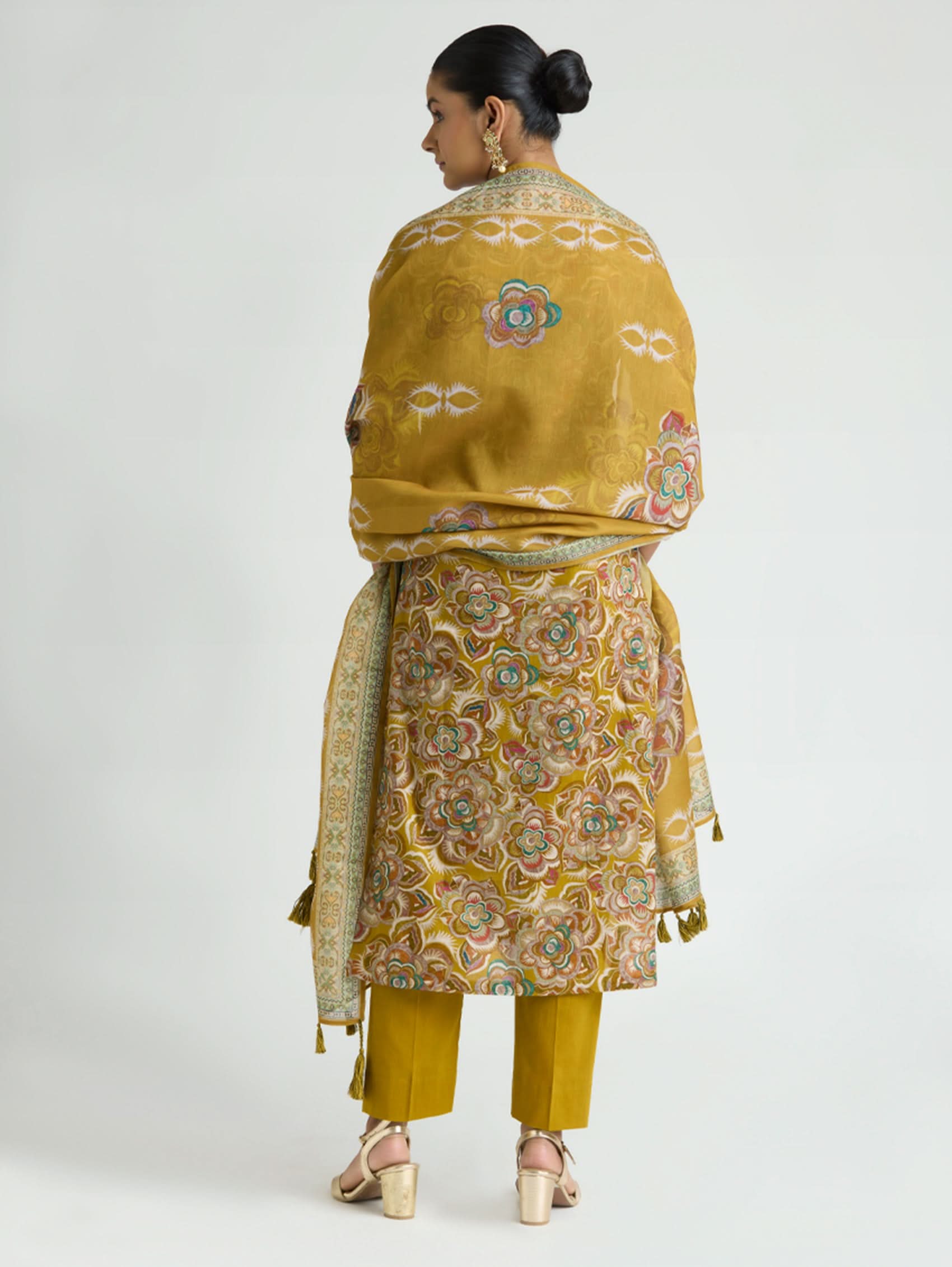 Woman wearing a mustard yellow traditional outfit with a patterned shawl on a white background