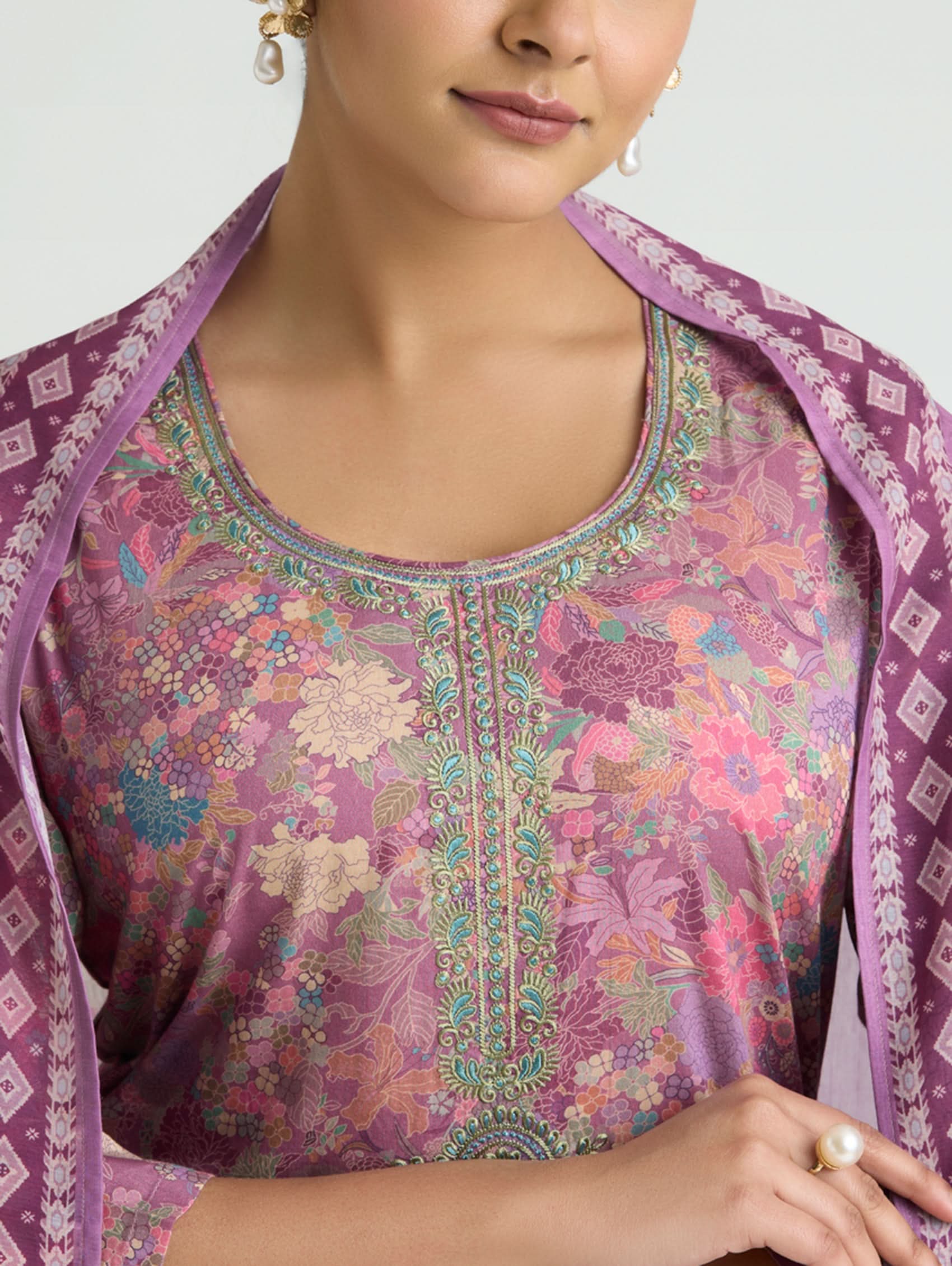 Woman wearing a patterned outfit with a purple shawl on a plain background