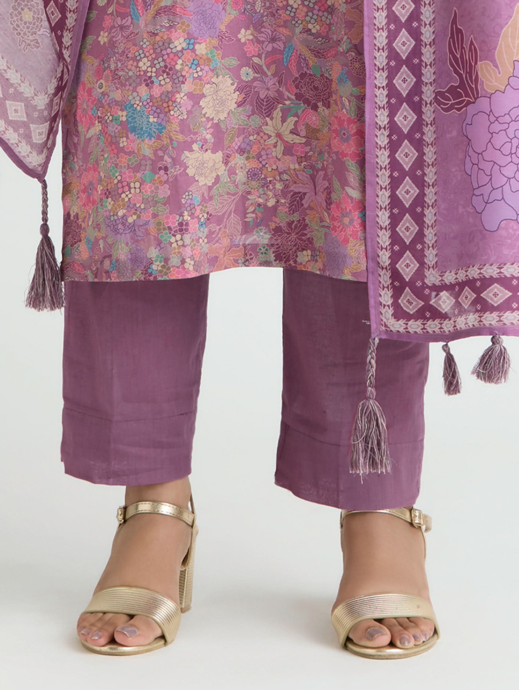 Purple traditional outfit with floral patterns and gold sandals on a white background