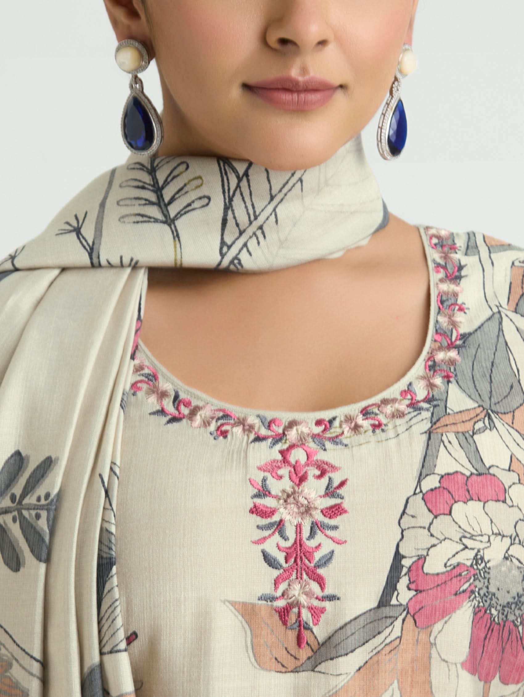 Woman wearing a floral embroidered top with a matching scarf and earrings on a white background