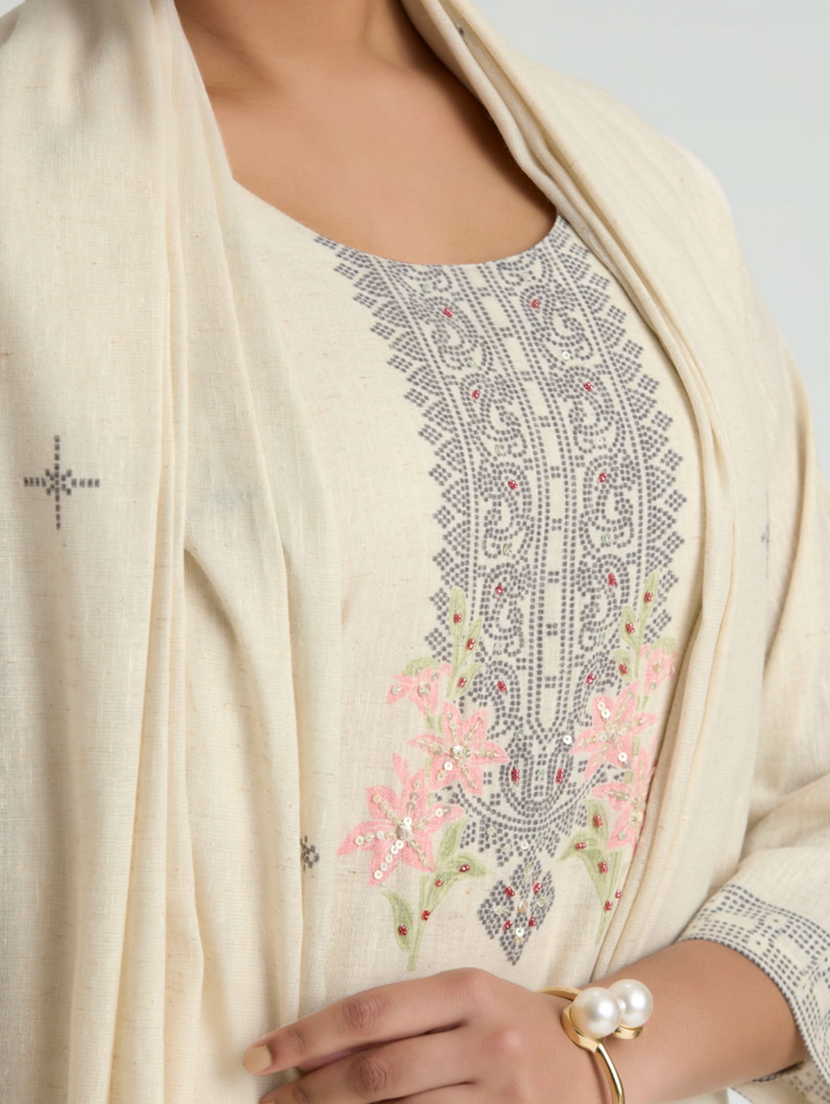 Close-up of a cream-colored embroidered garment with floral patterns on a plain background