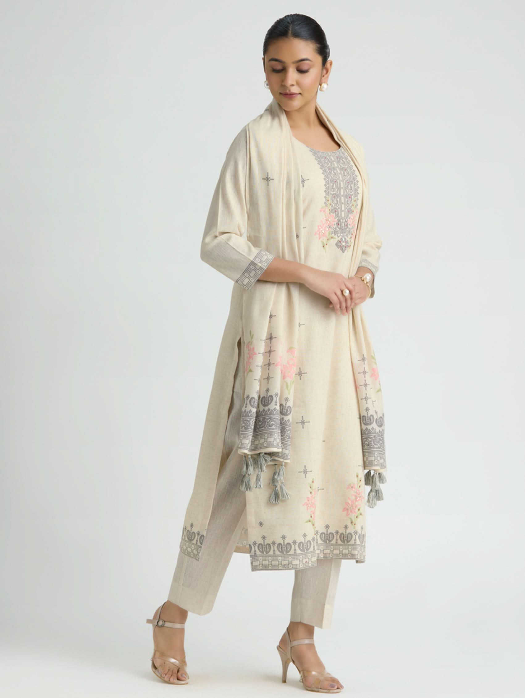 Woman wearing a cream-colored traditional outfit with floral embroidery on a white background