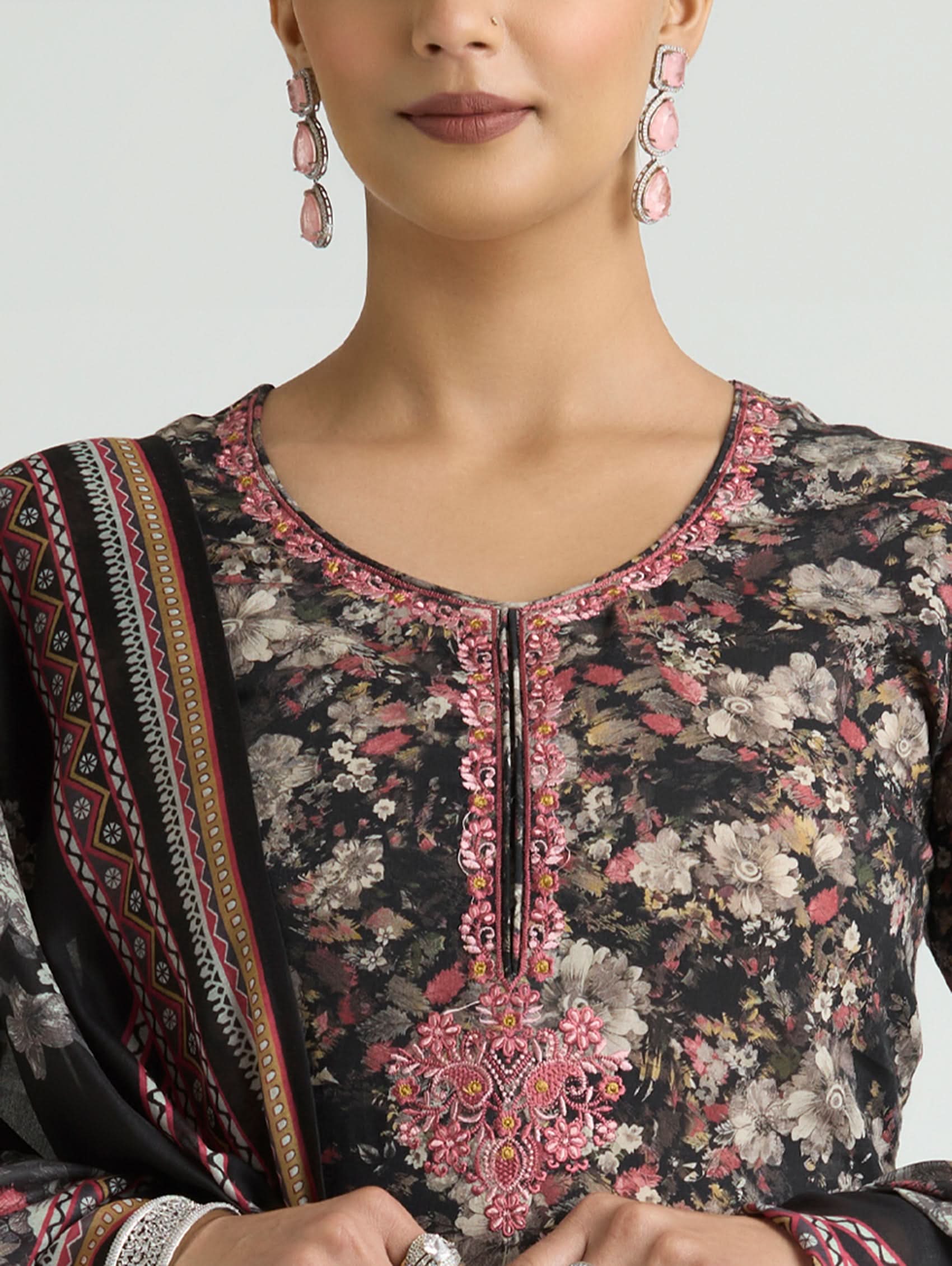 Close-up of a person wearing a floral and embroidered traditional outfit with a neutral background