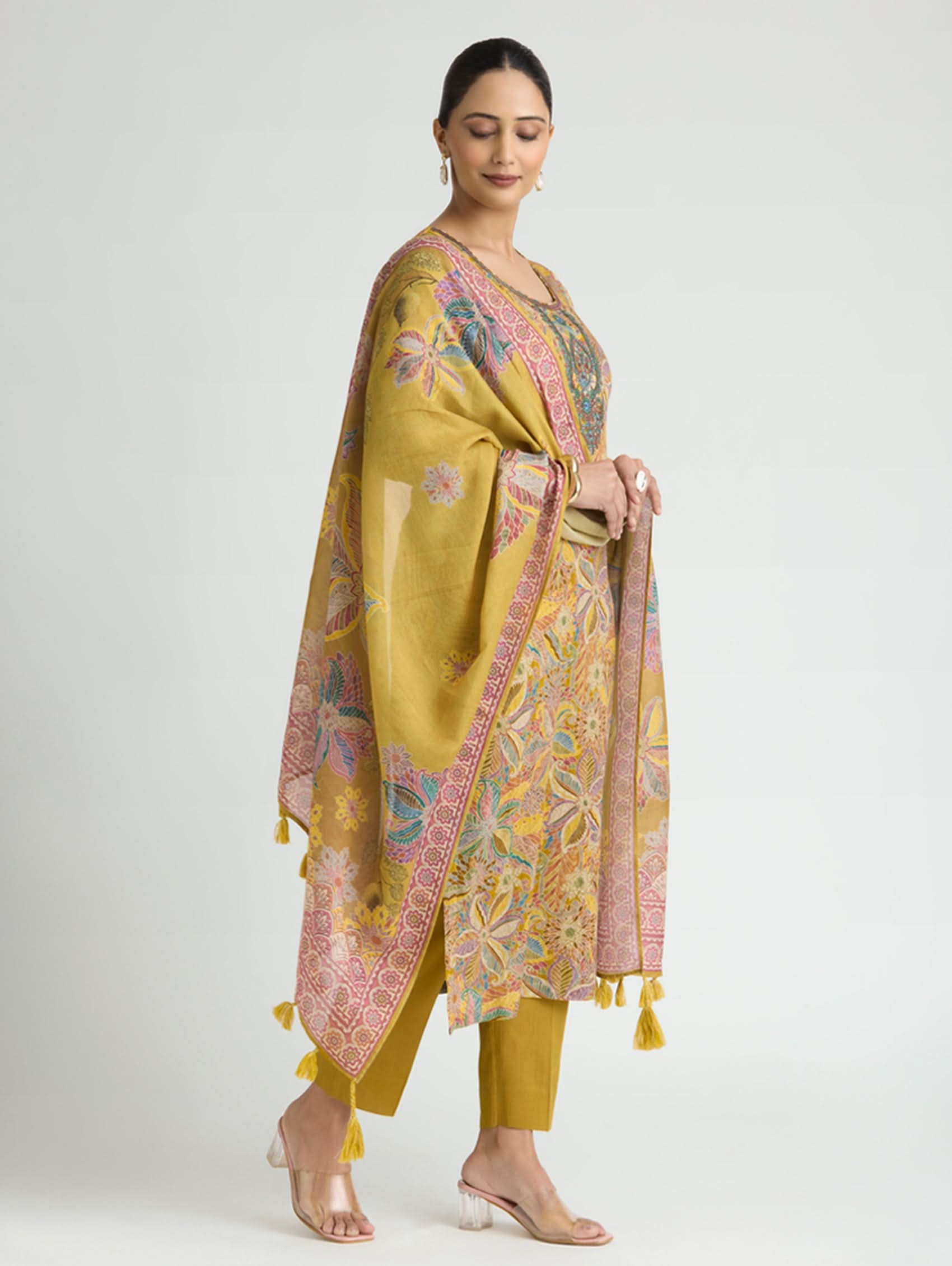 Woman wearing a mustard yellow traditional outfit with a patterned dupatta on a white background