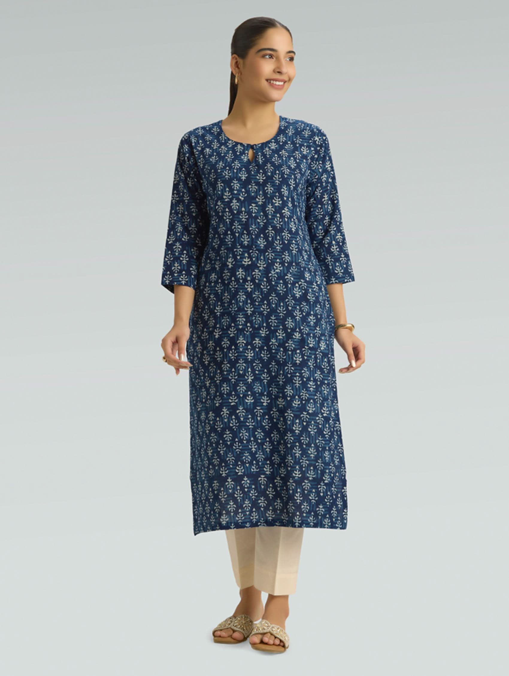 Woman wearing a blue floral kurta with beige pants on a gray background