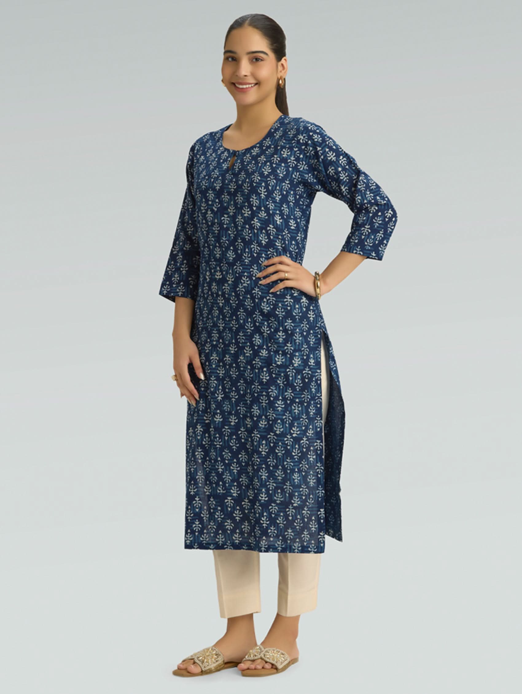 Woman wearing a blue floral kurta with beige pants on a light gray background