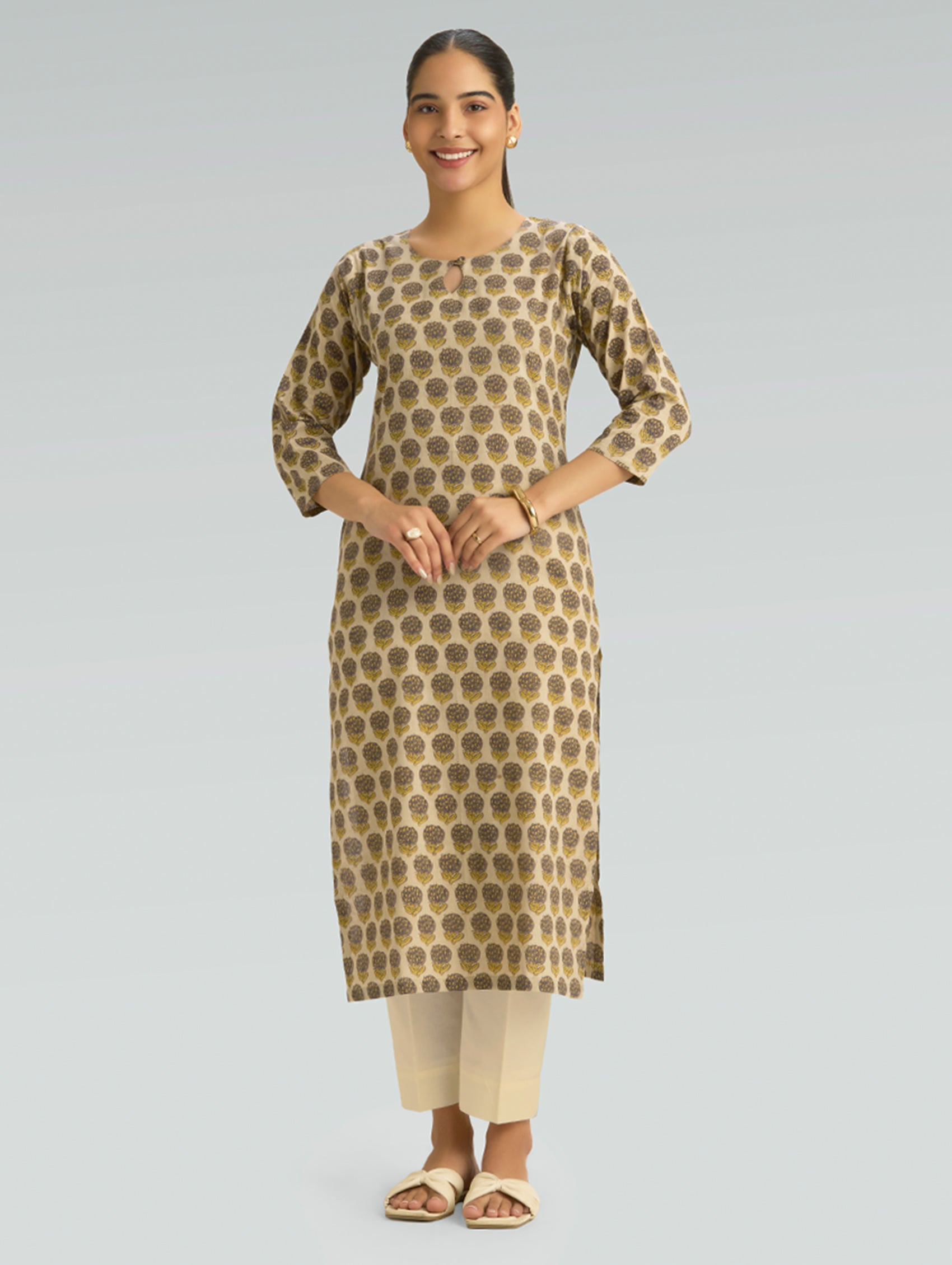 Woman wearing a patterned kurta with beige pants on a gray background