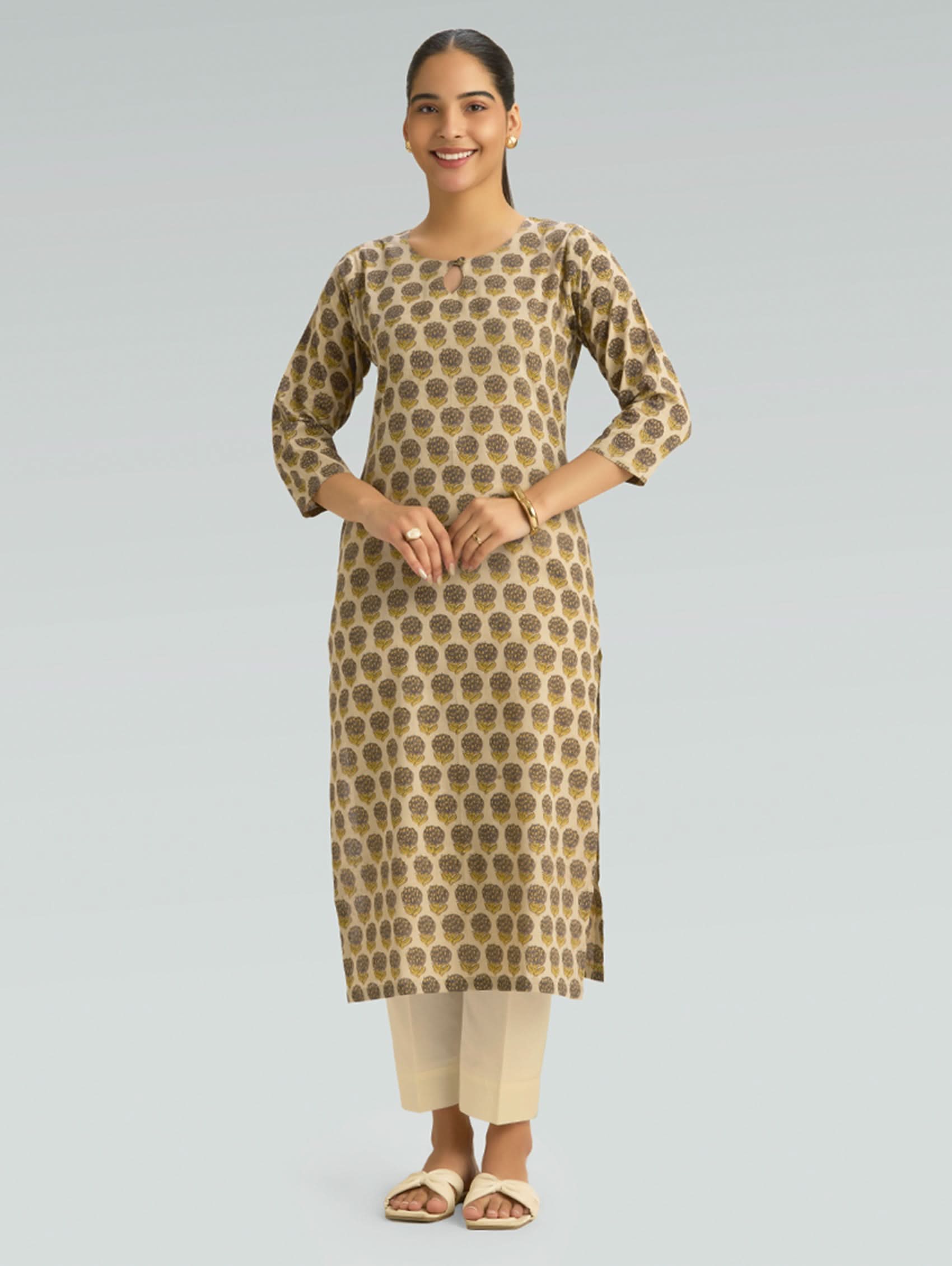 Woman wearing a patterned kurta with beige pants on a gray background