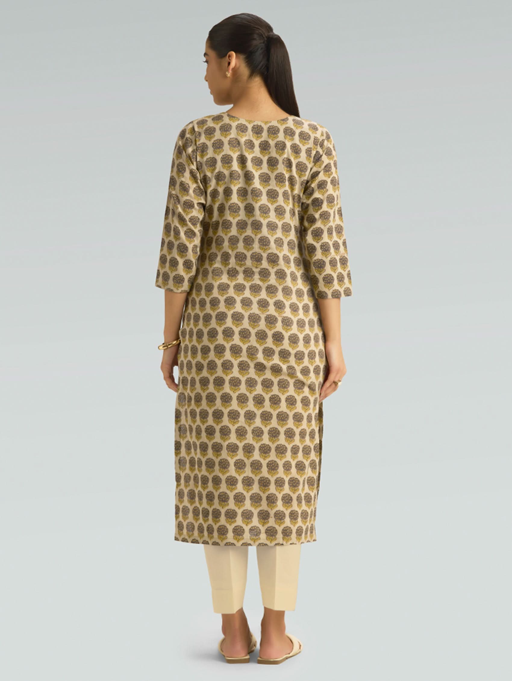 Woman wearing a patterned kurta with beige pants on a gray background
