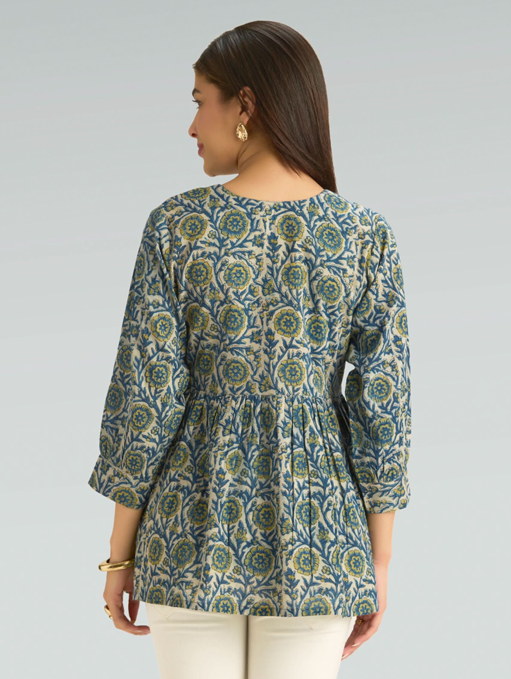 Woman wearing a patterned green and blue top on a gray background