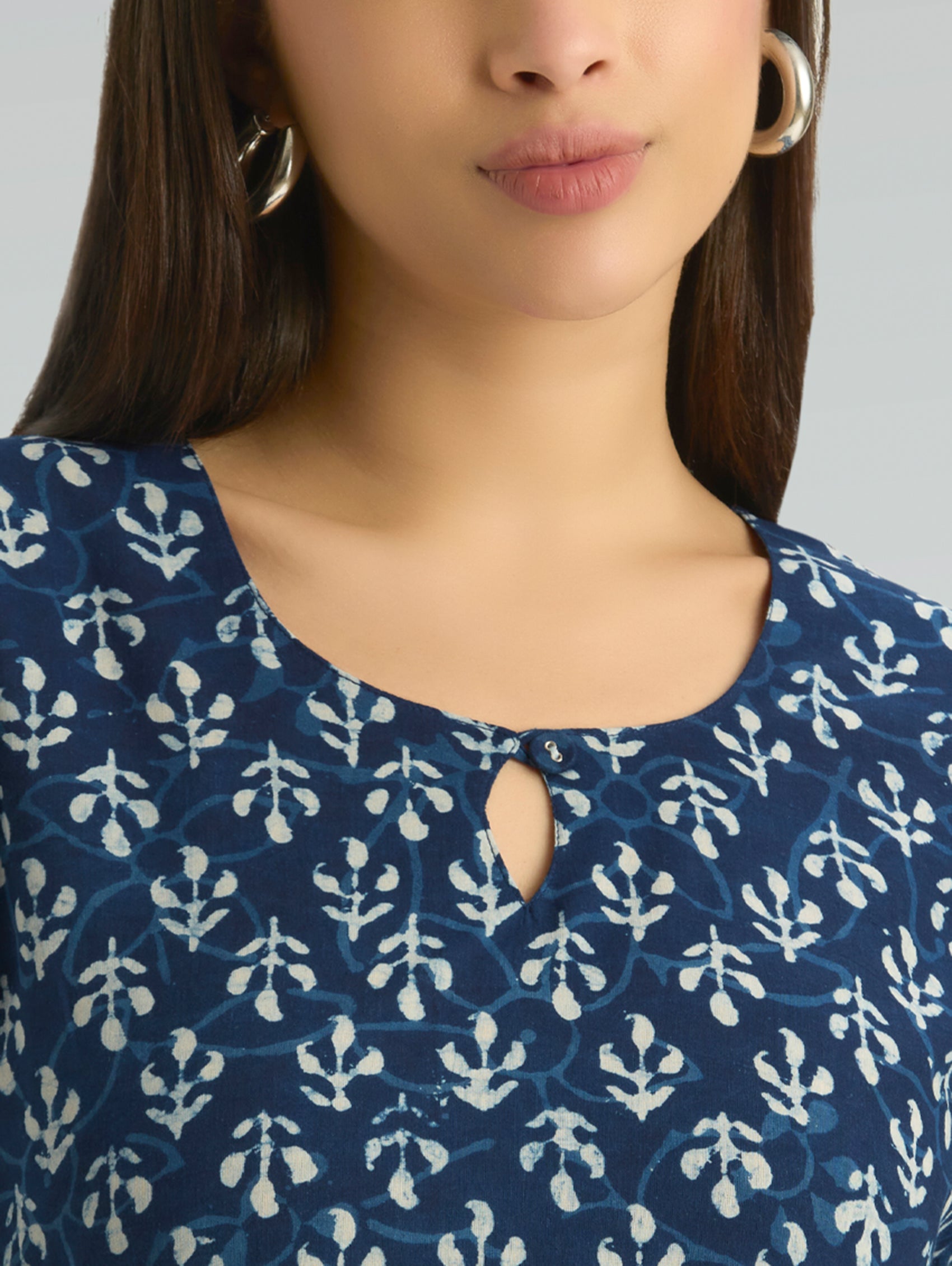 Close-up of a person wearing a blue and white patterned top with a plain background