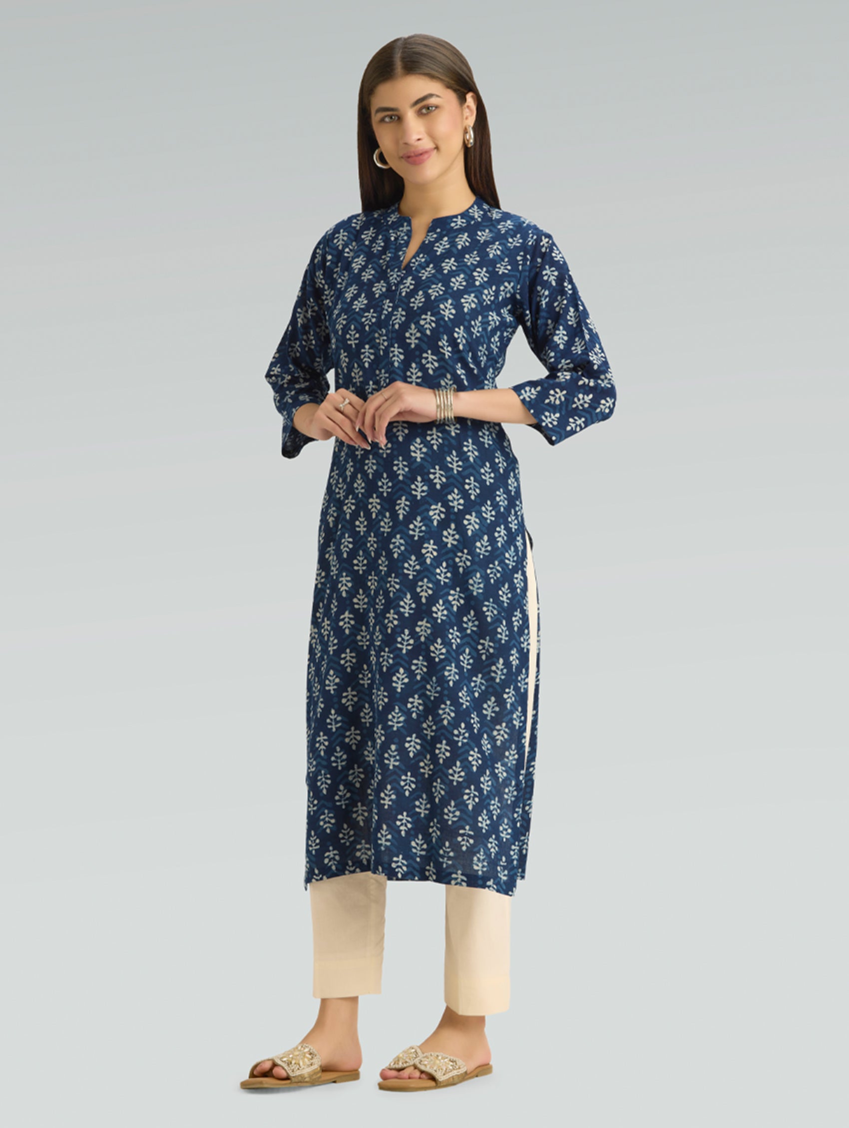 Woman wearing a blue floral kurta with beige pants on a gray background