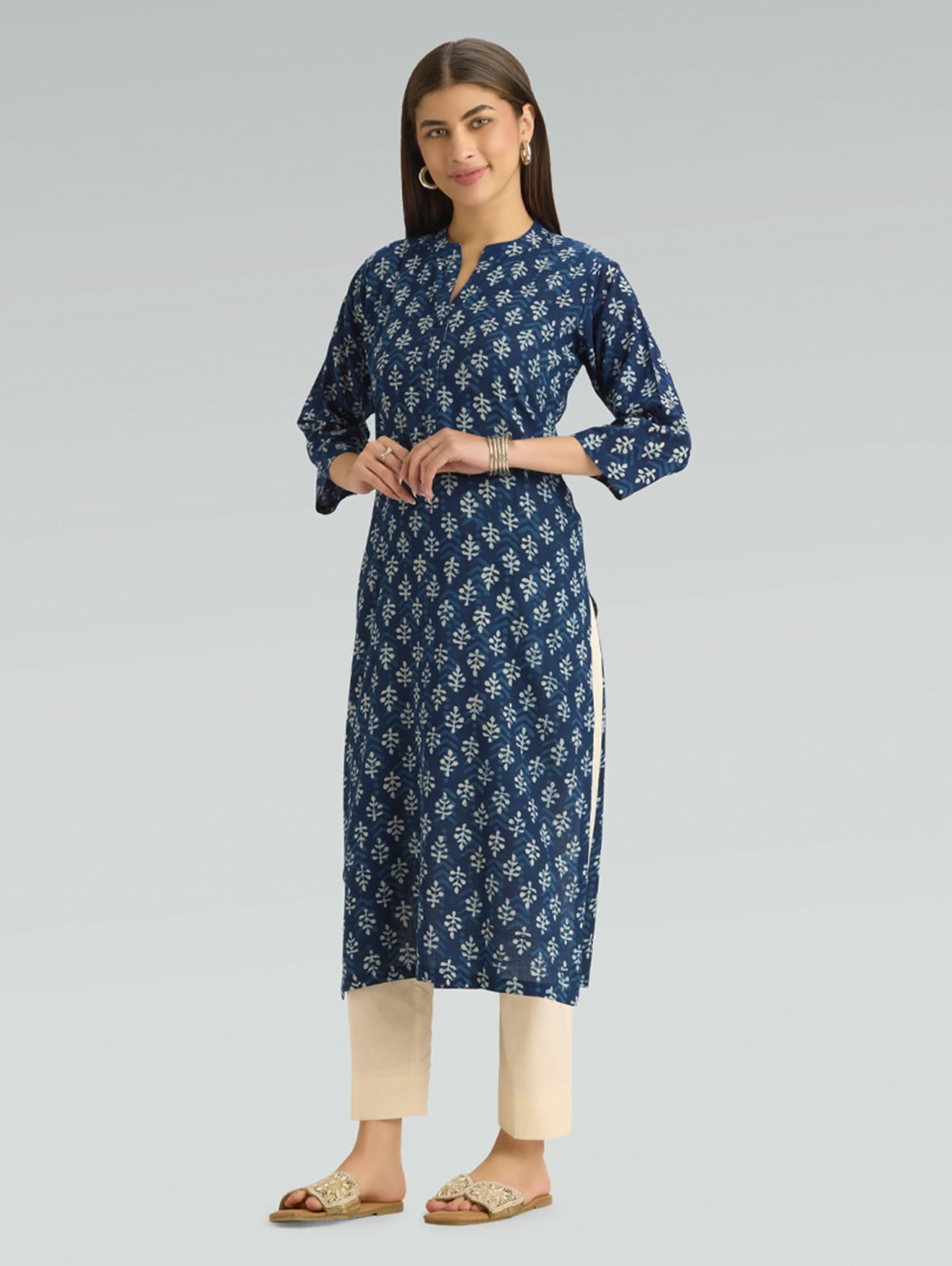 Woman wearing a blue floral kurta with beige pants on a gray background