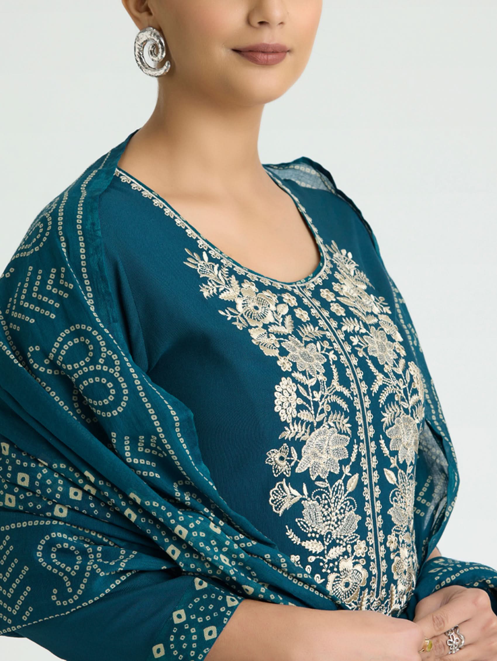 Teal embroidered garment with white patterns on a neutral background