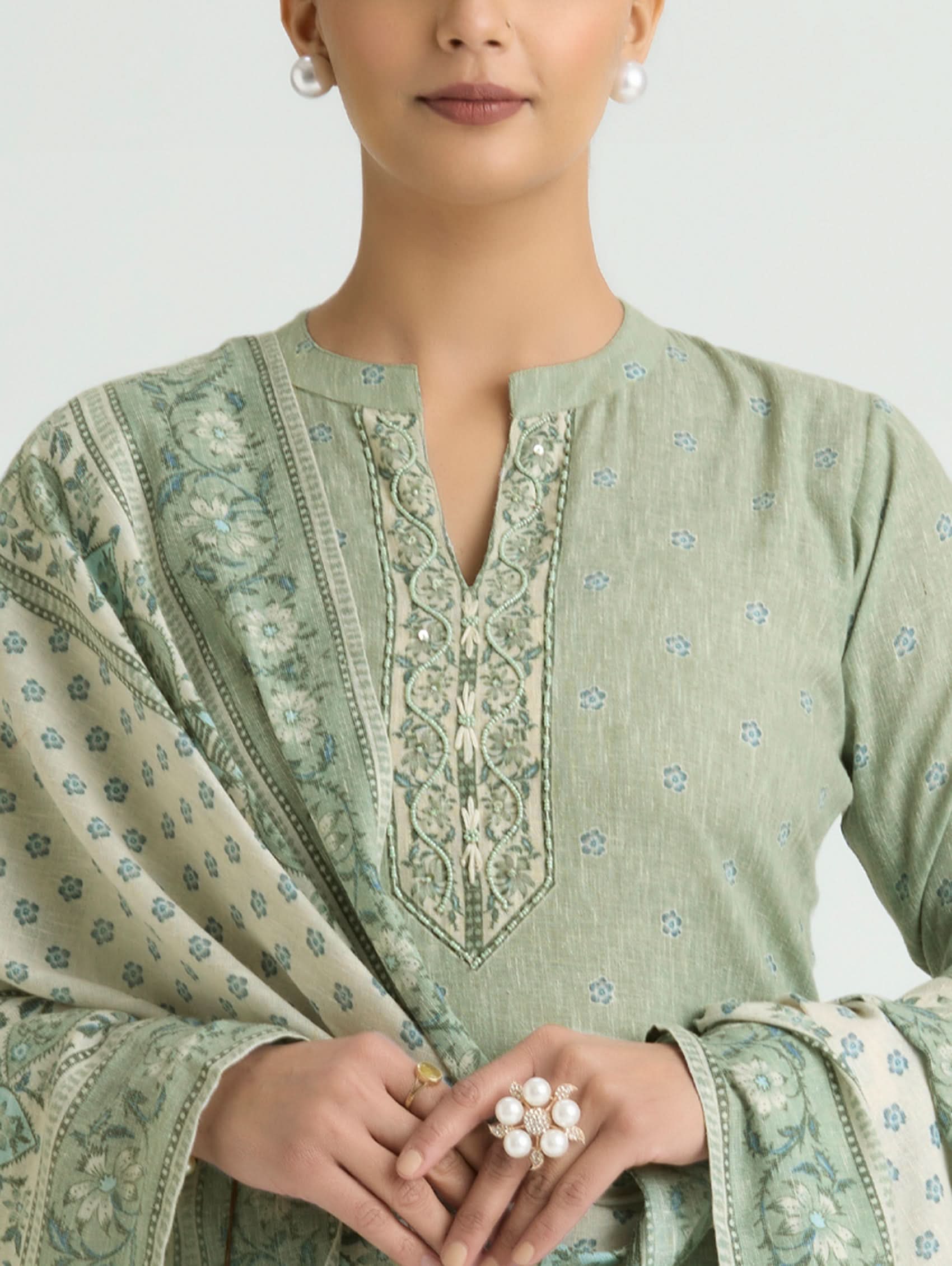 Woman wearing a green embroidered traditional outfit with a plain background