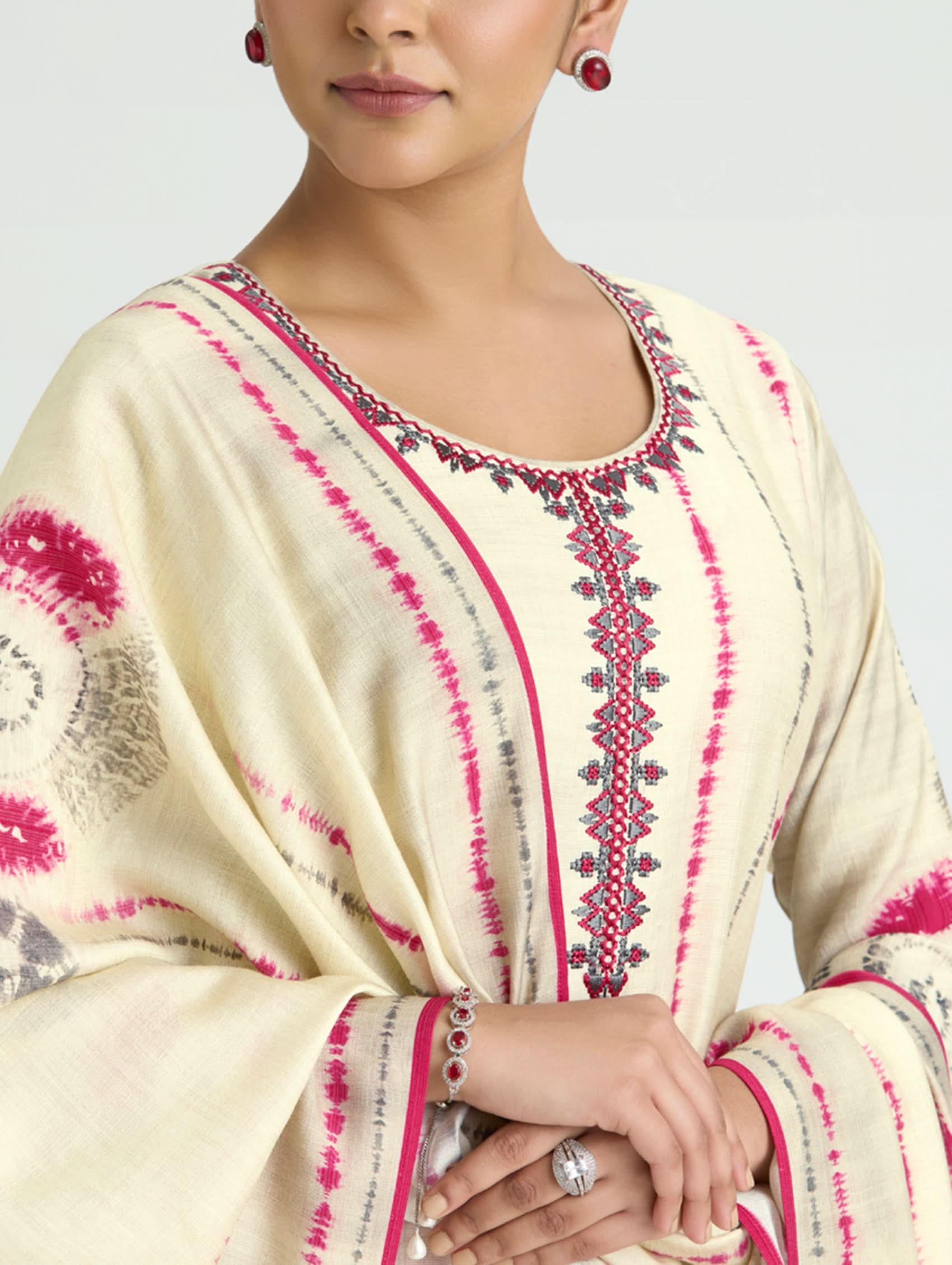 Woman wearing a cream-colored traditional outfit with pink and red patterns on a plain background