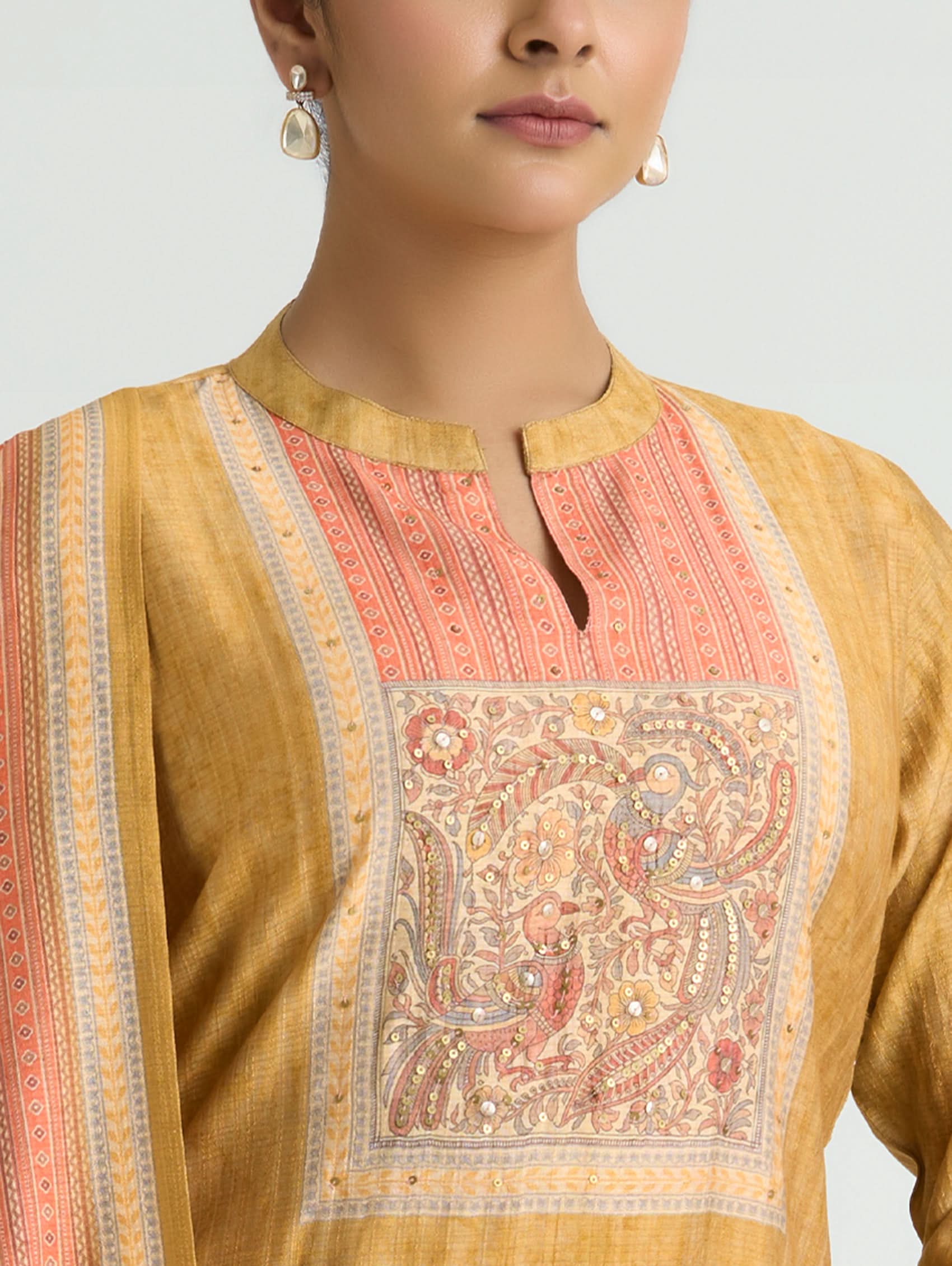 Close-up of a mustard yellow kurta with intricate pink and white embroidery on a plain background