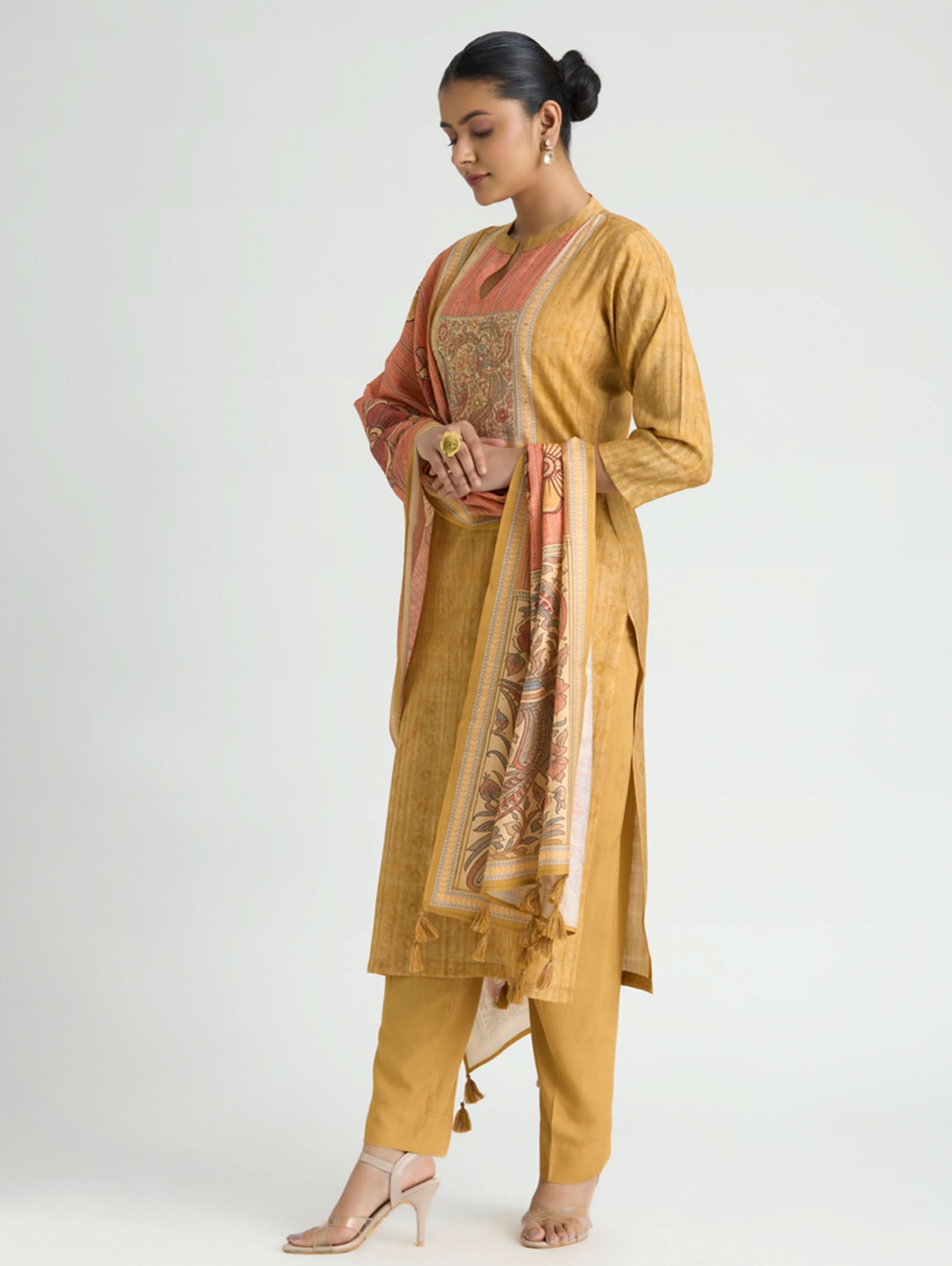 Woman wearing a mustard yellow traditional outfit with a pink dupatta on a white background