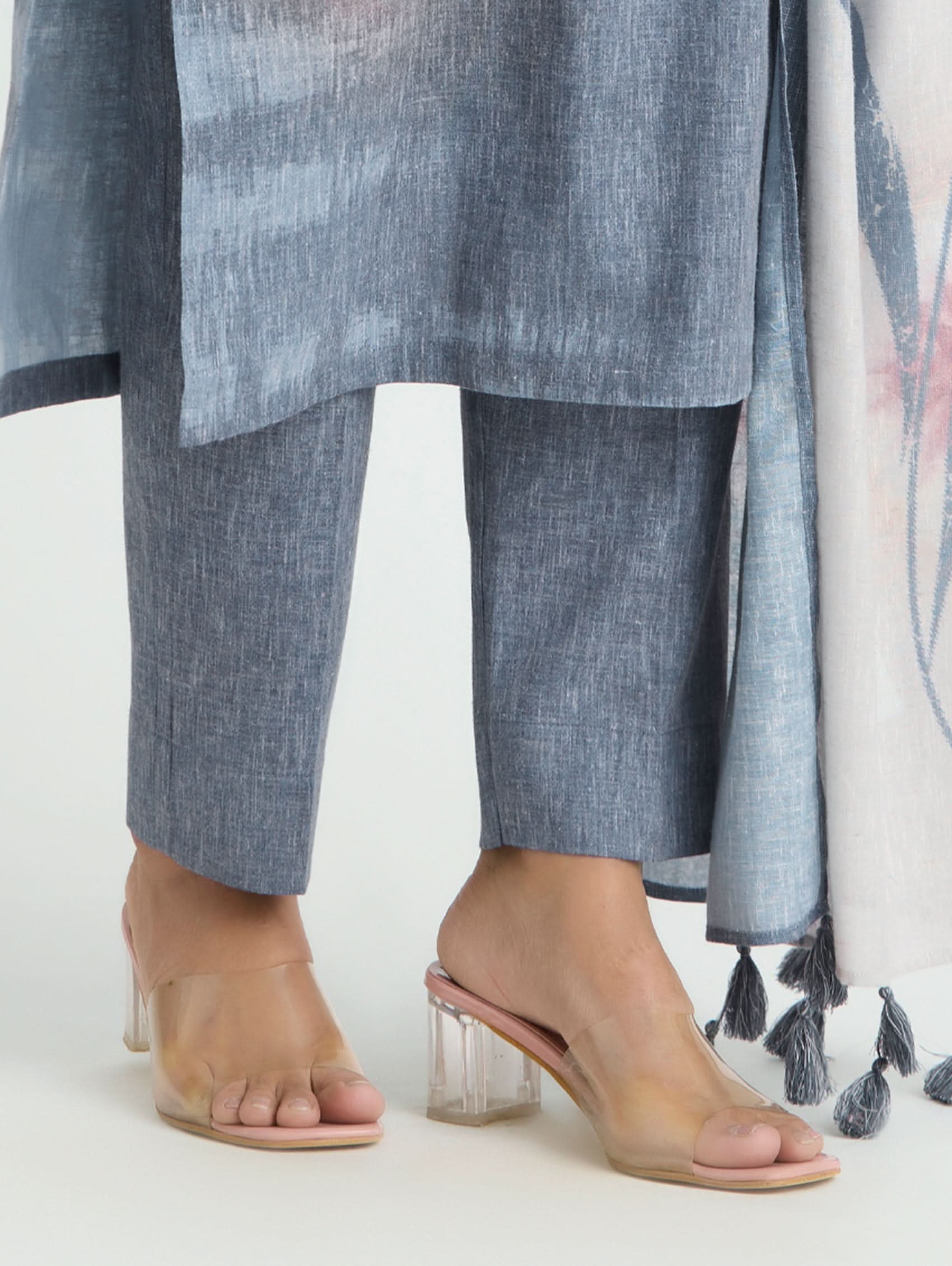 Clear high-heeled sandals worn with a blue outfit on a white background