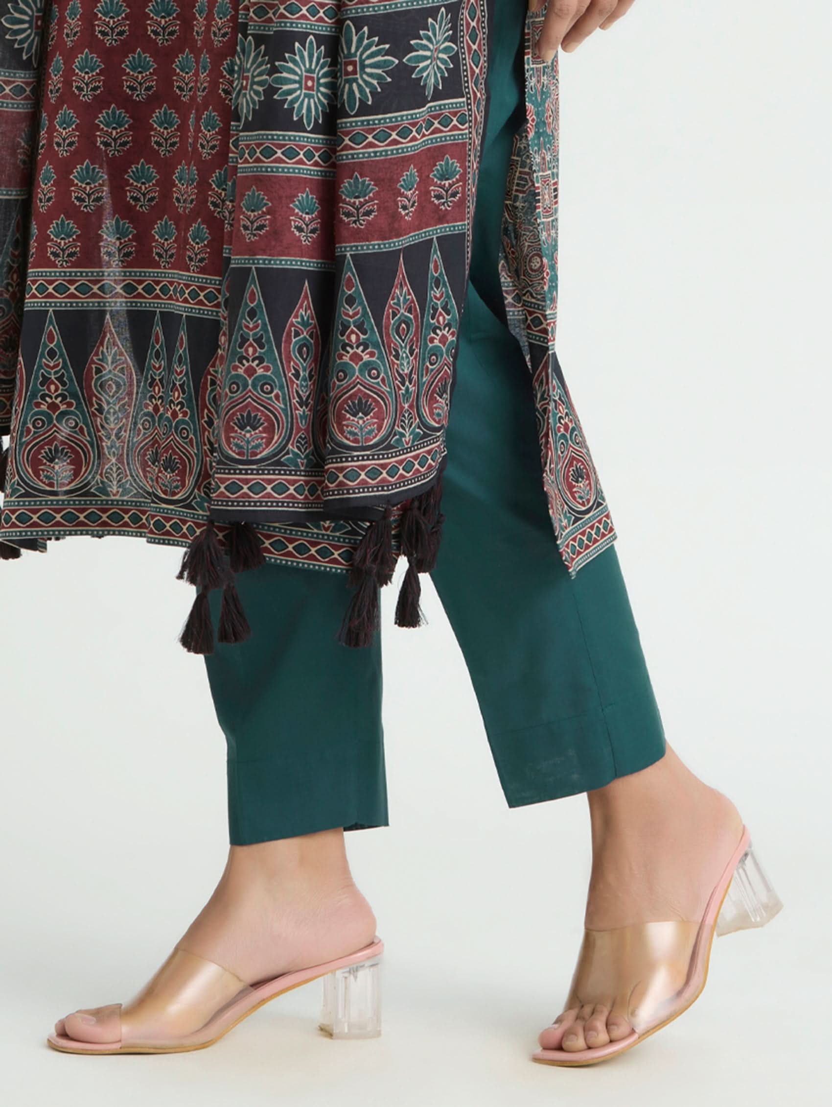 Person wearing a patterned scarf and green pants with transparent sandals on a white background