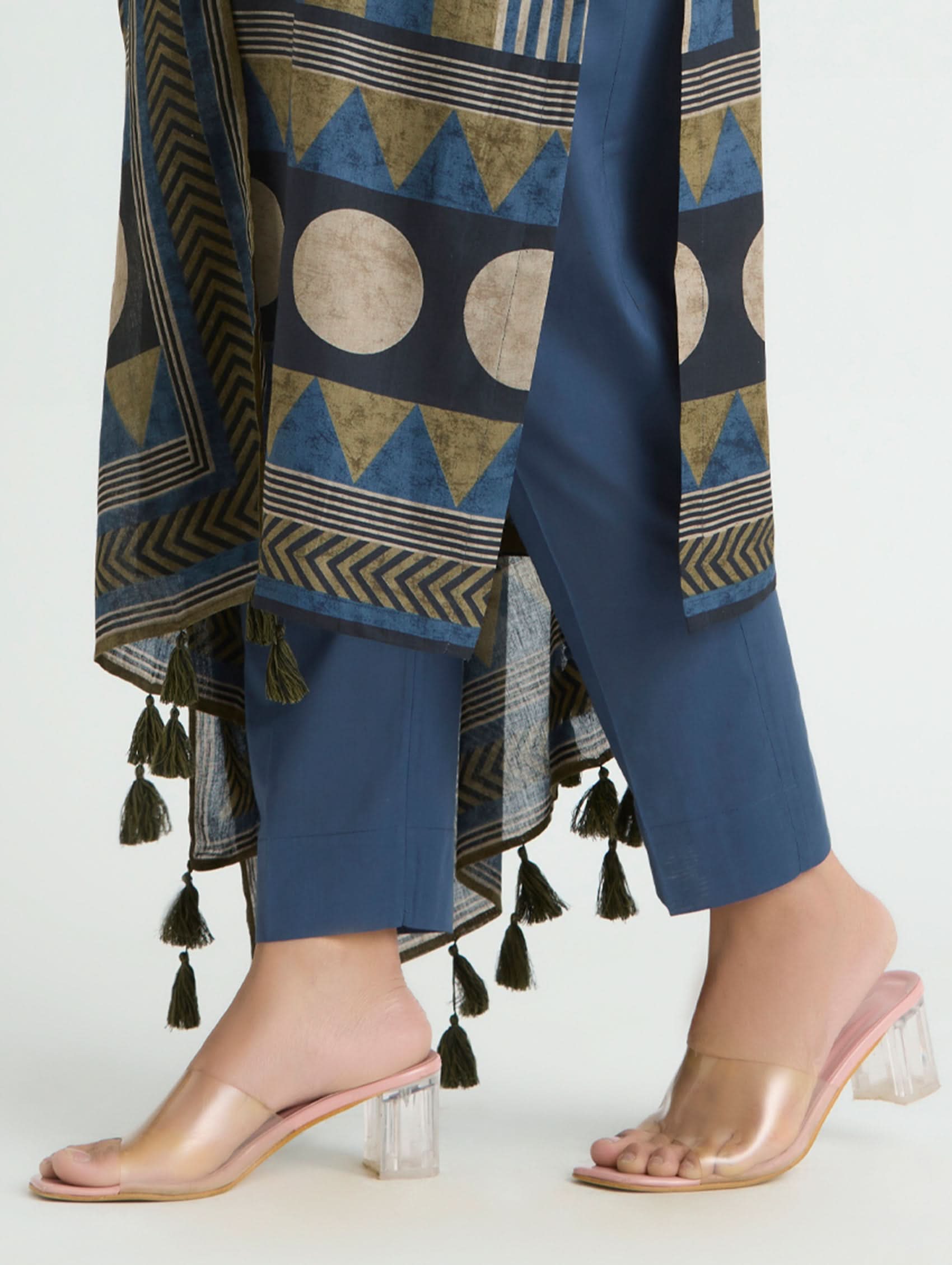 Person wearing blue pants with geometric patterns and a matching top, paired with clear high-heeled sandals on a white background.