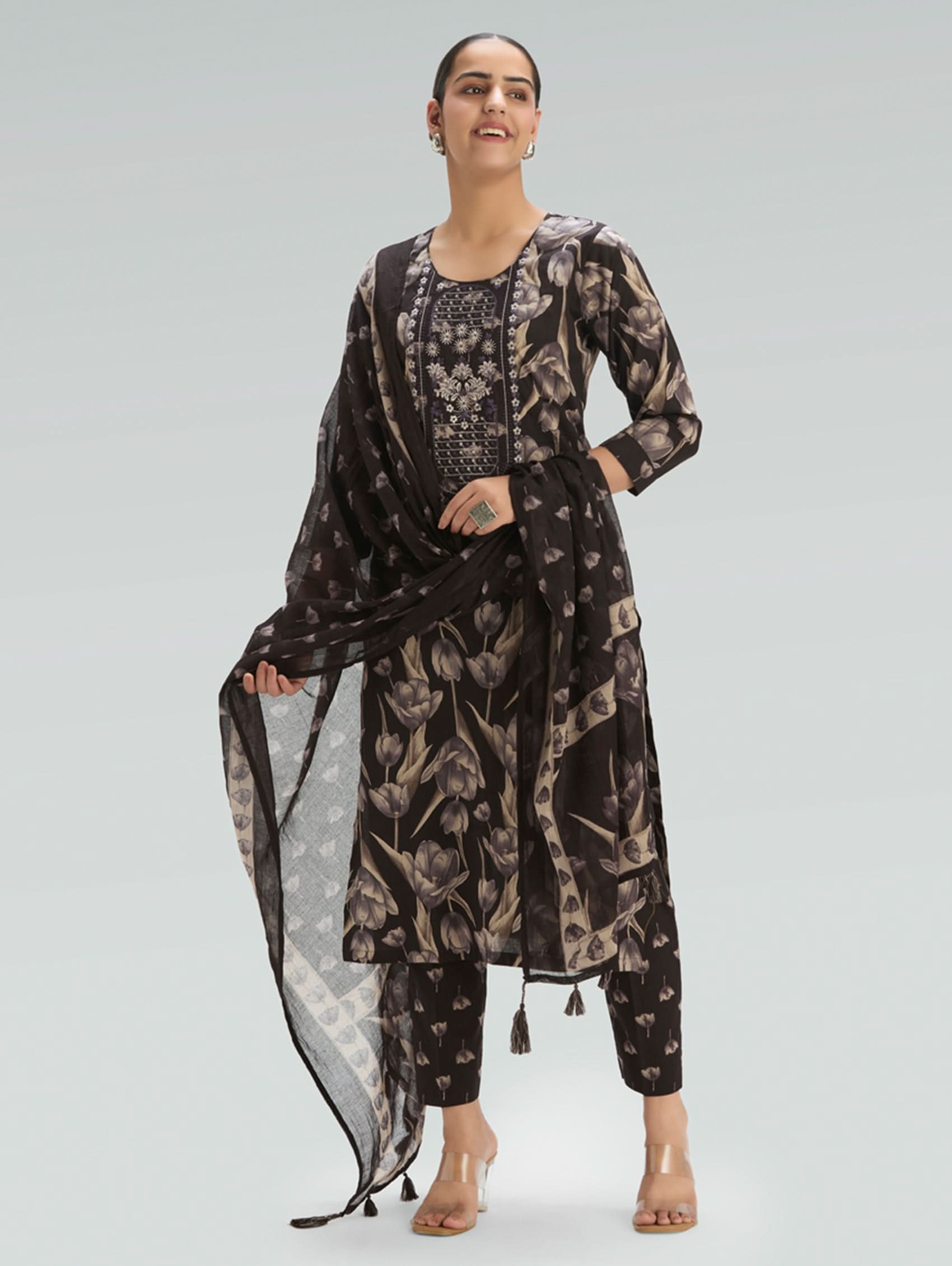 Woman wearing a black floral outfit with a sheer dupatta on a light gray background