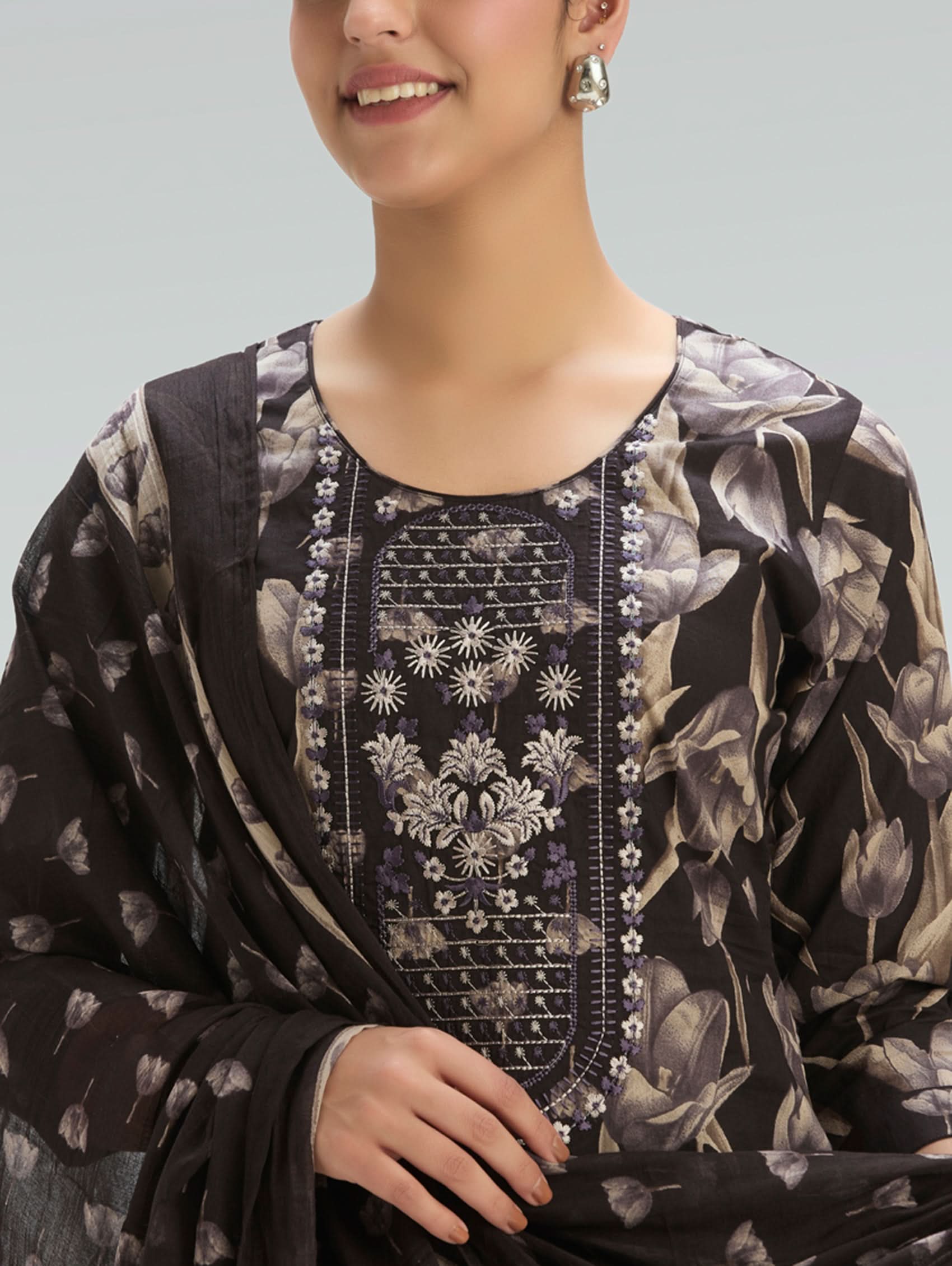 Woman wearing a dark floral dress with intricate embroidery on a light gray background