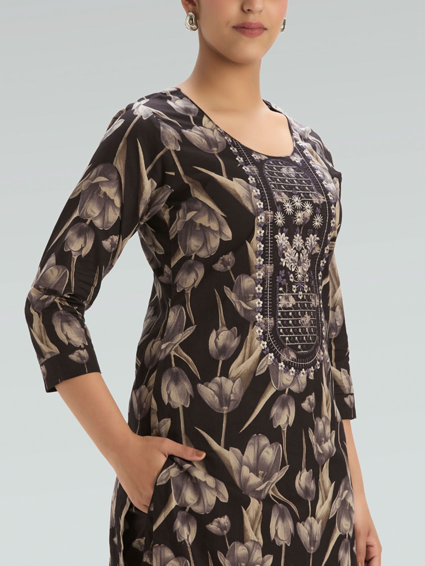 Woman wearing a black floral dress with intricate patterns on a light gray background