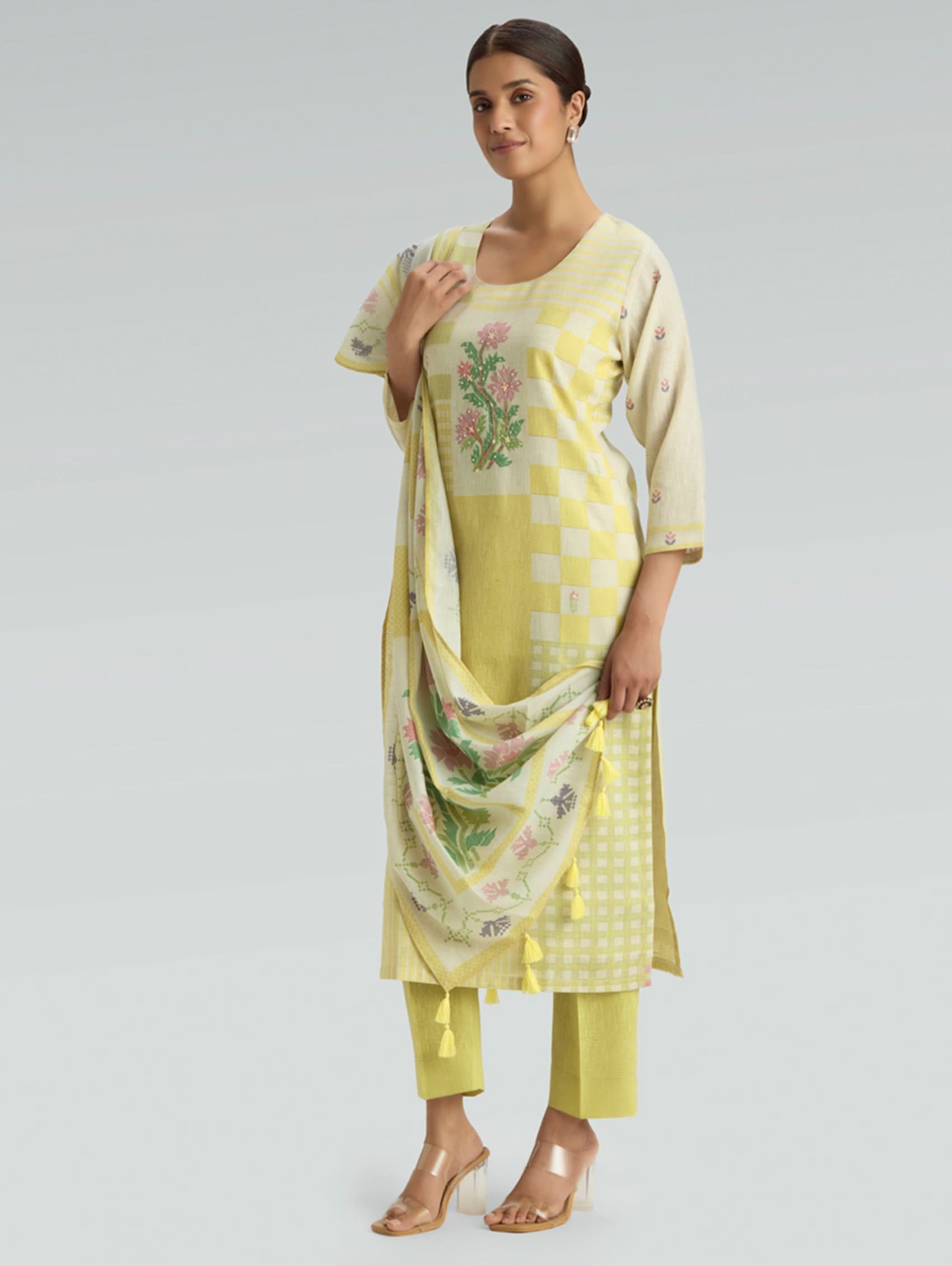 Woman wearing a yellow traditional outfit with a floral dupatta on a light gray background