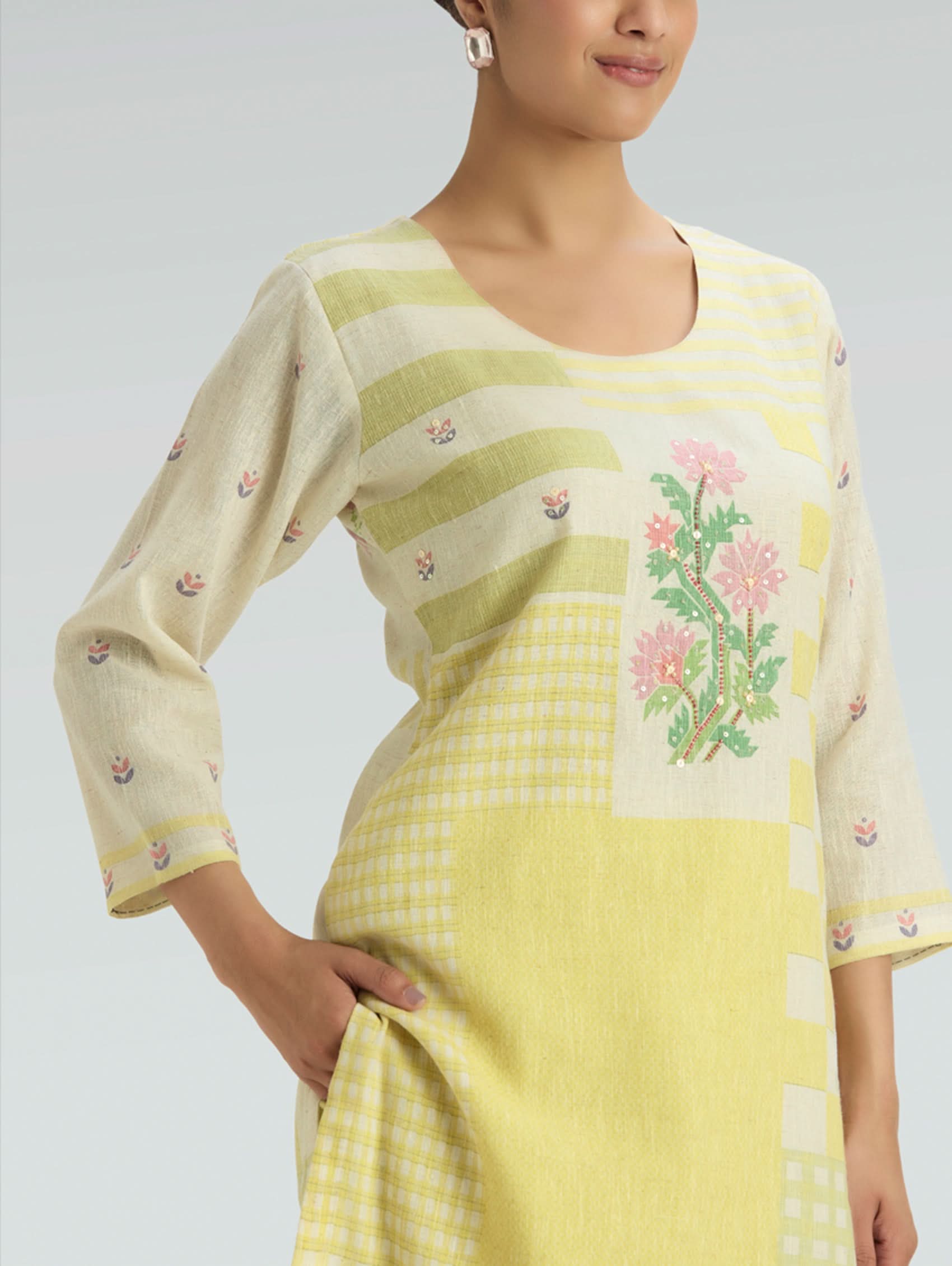 Woman wearing a yellow and white embroidered traditional outfit on a plain background