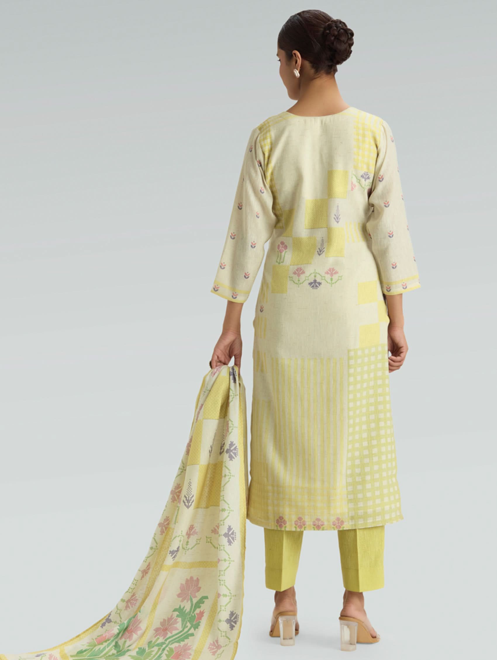 Woman wearing a light yellow traditional outfit with a floral dupatta on a plain background