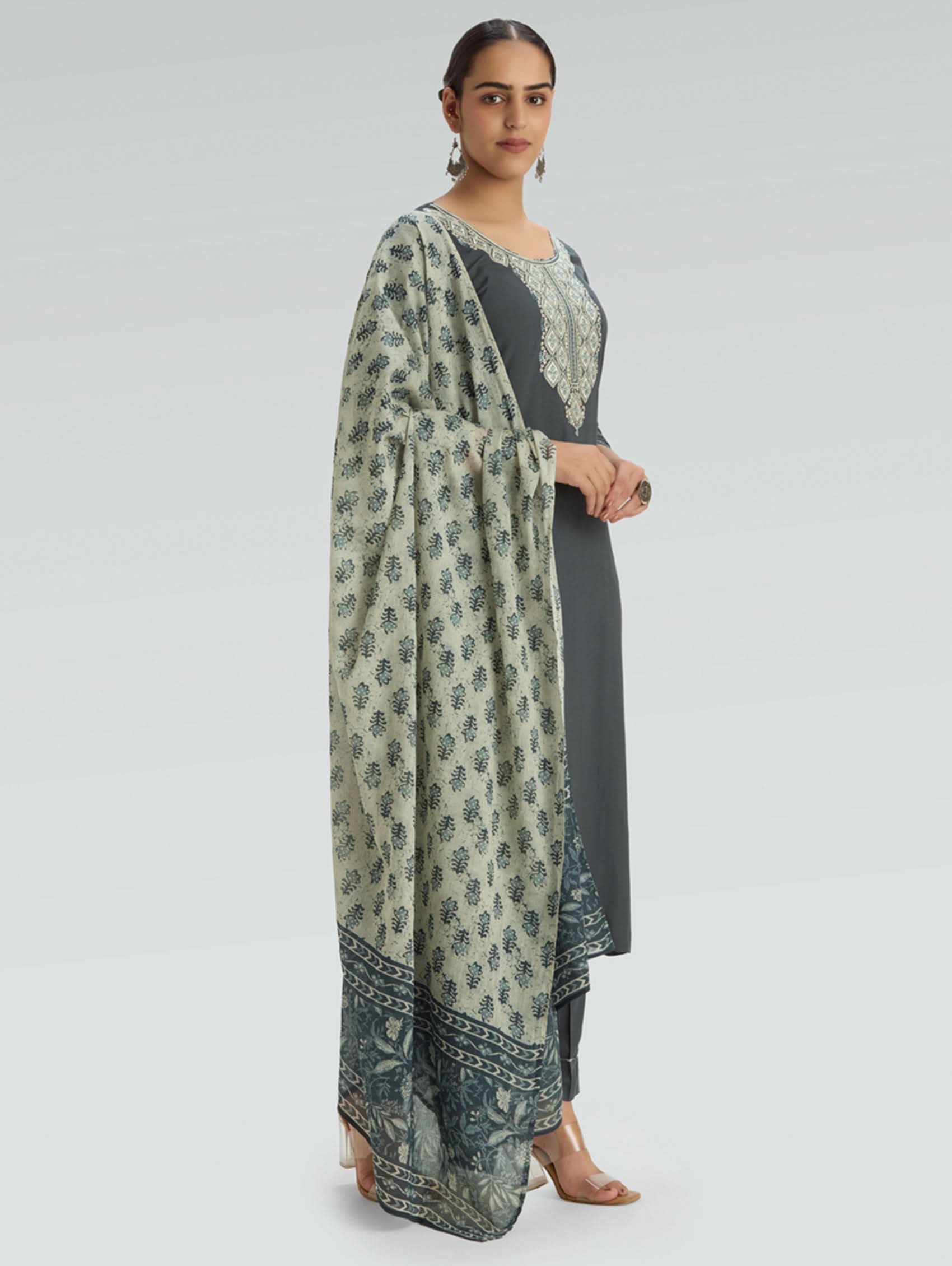 Woman wearing a long floral-patterned scarf over a dark outfit on a light gray background