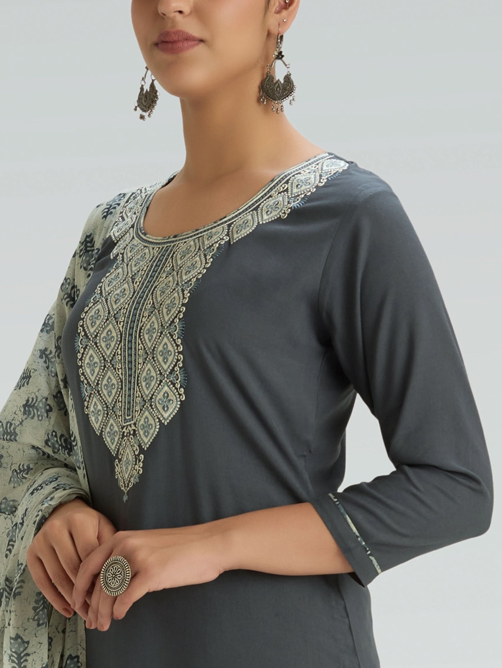 Woman wearing a dark gray top with intricate white embroidery on a light gray background