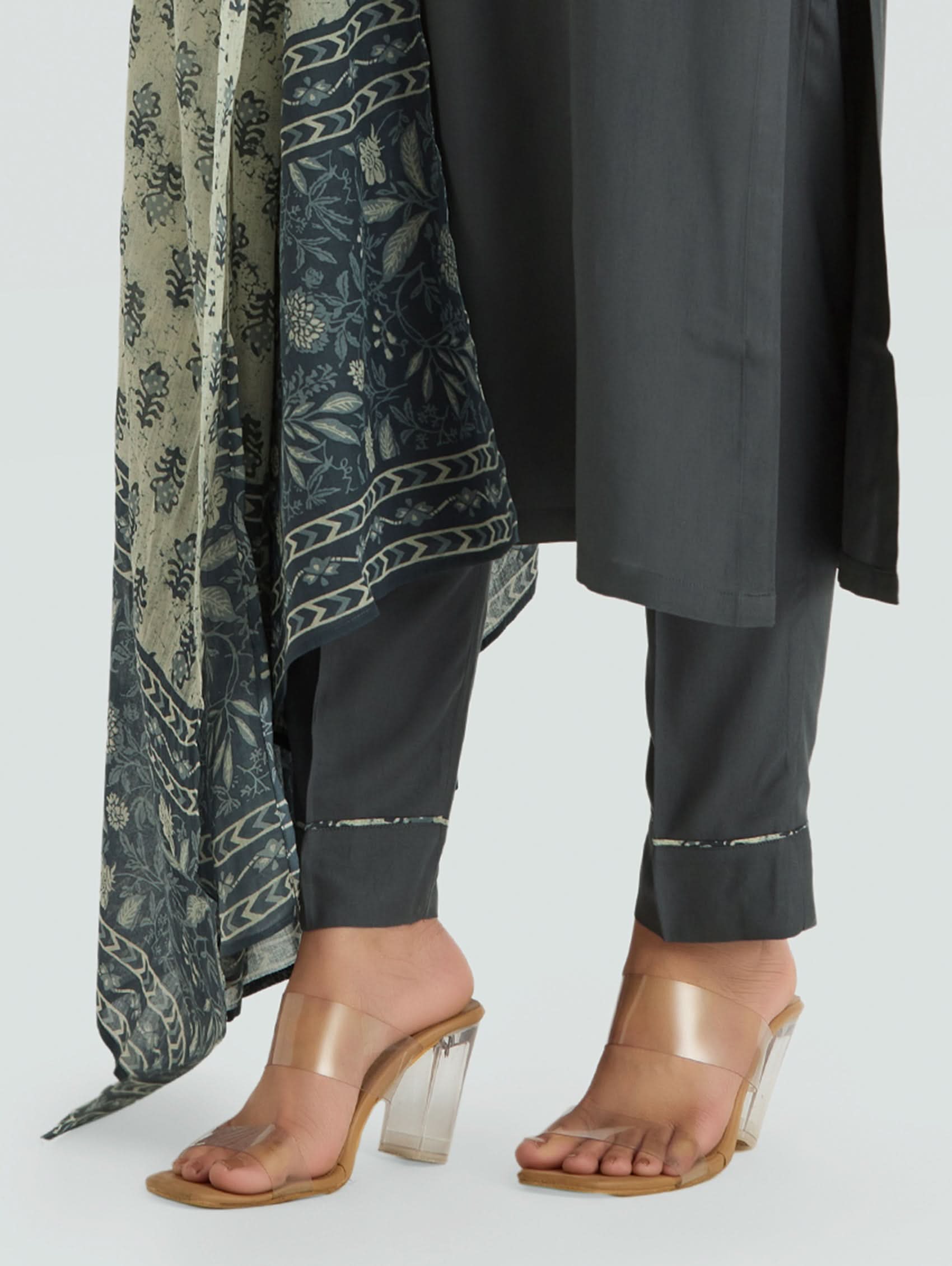 Person wearing a long patterned scarf, black outfit, and transparent high-heeled sandals on a light gray background