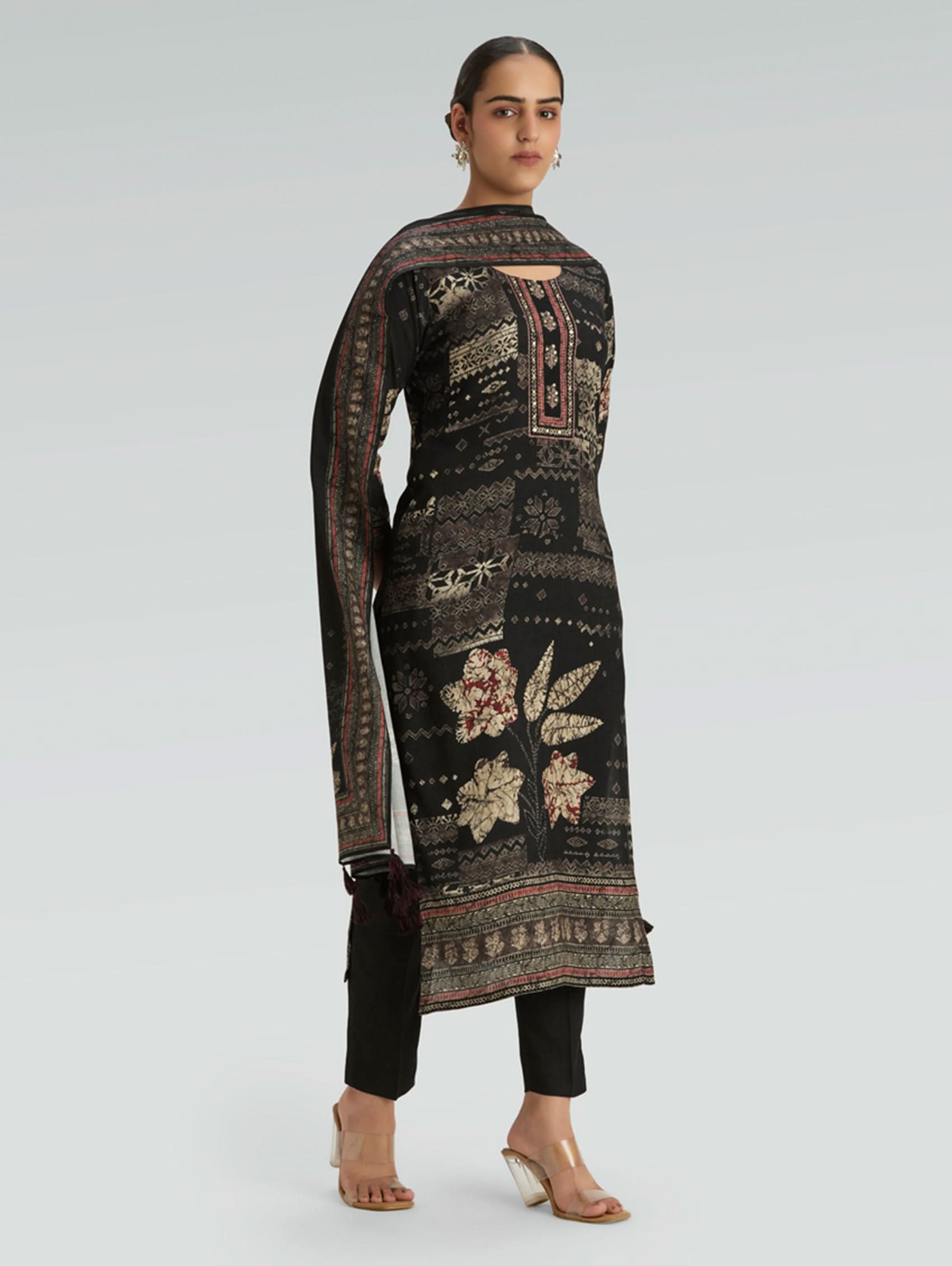 Woman wearing a long, dark-colored embroidered dress with floral patterns on a light gray background