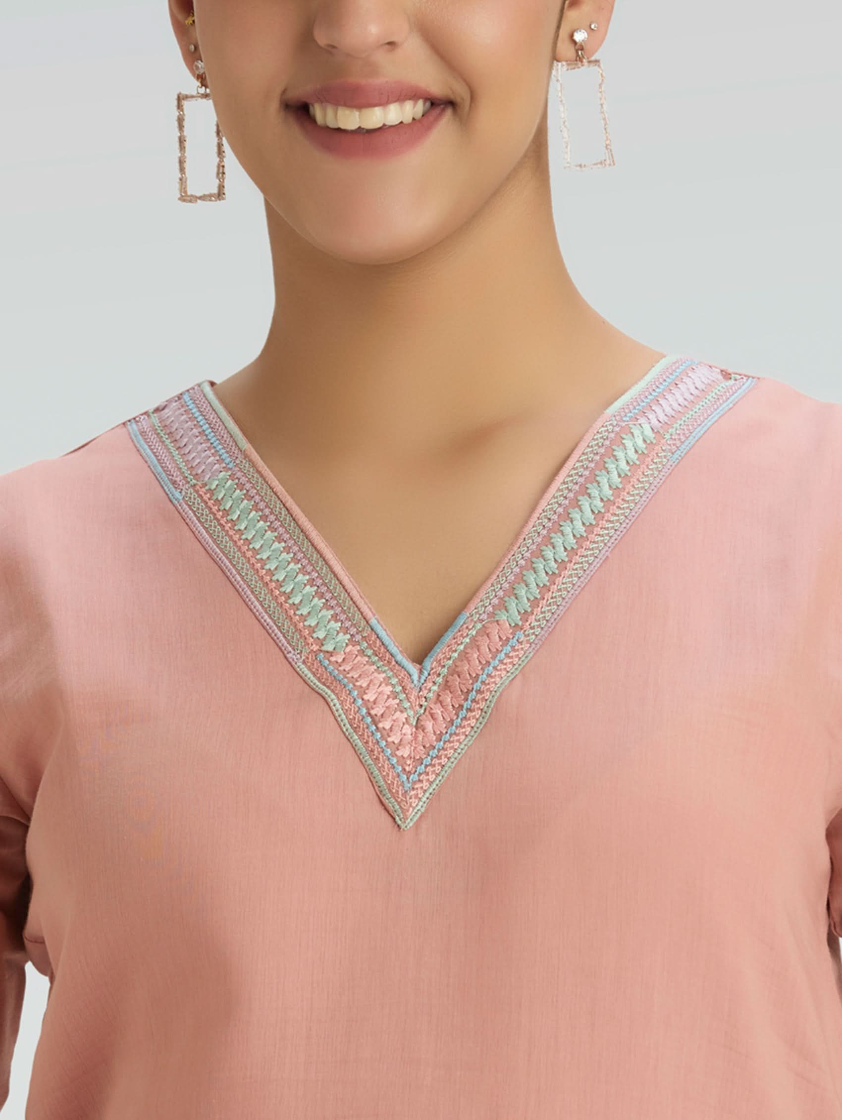 Close-up of a pink top with intricate embroidery on a light gray background