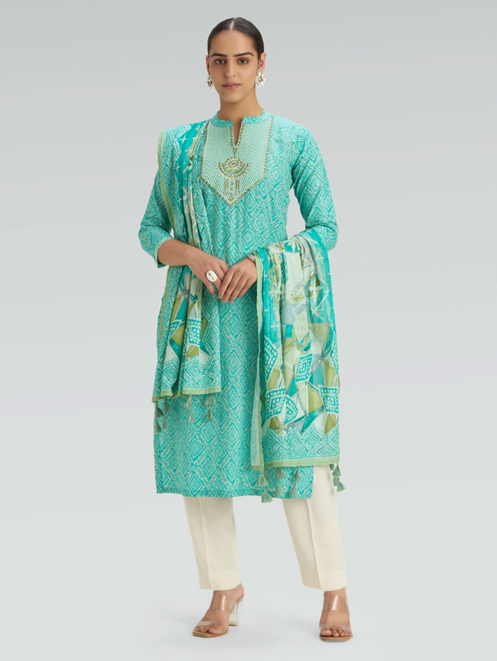 Woman wearing a teal traditional outfit with a matching dupatta on a gray background