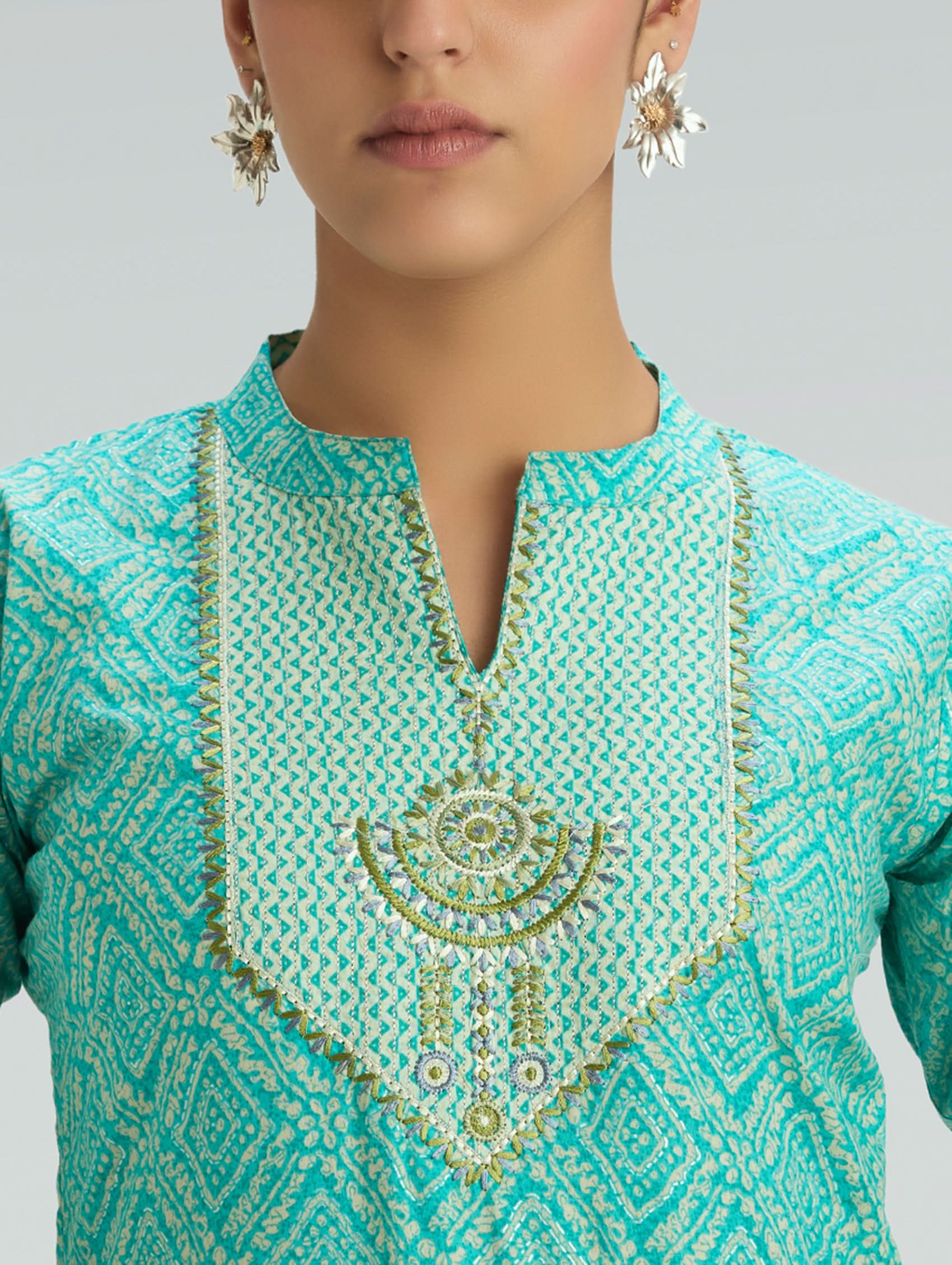 Close-up of a turquoise embroidered garment with gold patterns on a neutral background