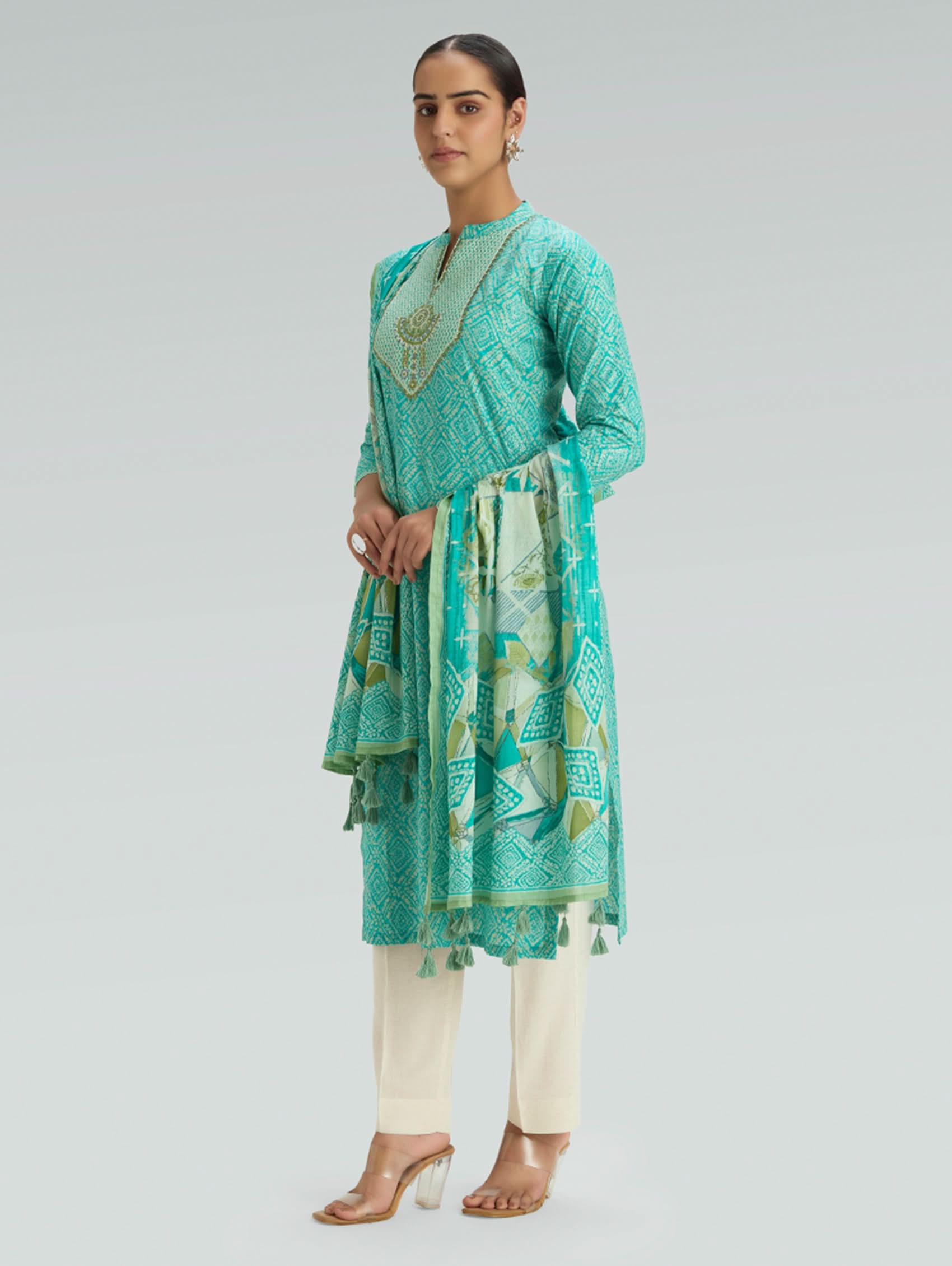 Woman wearing a teal traditional outfit with a matching dupatta on a gray background