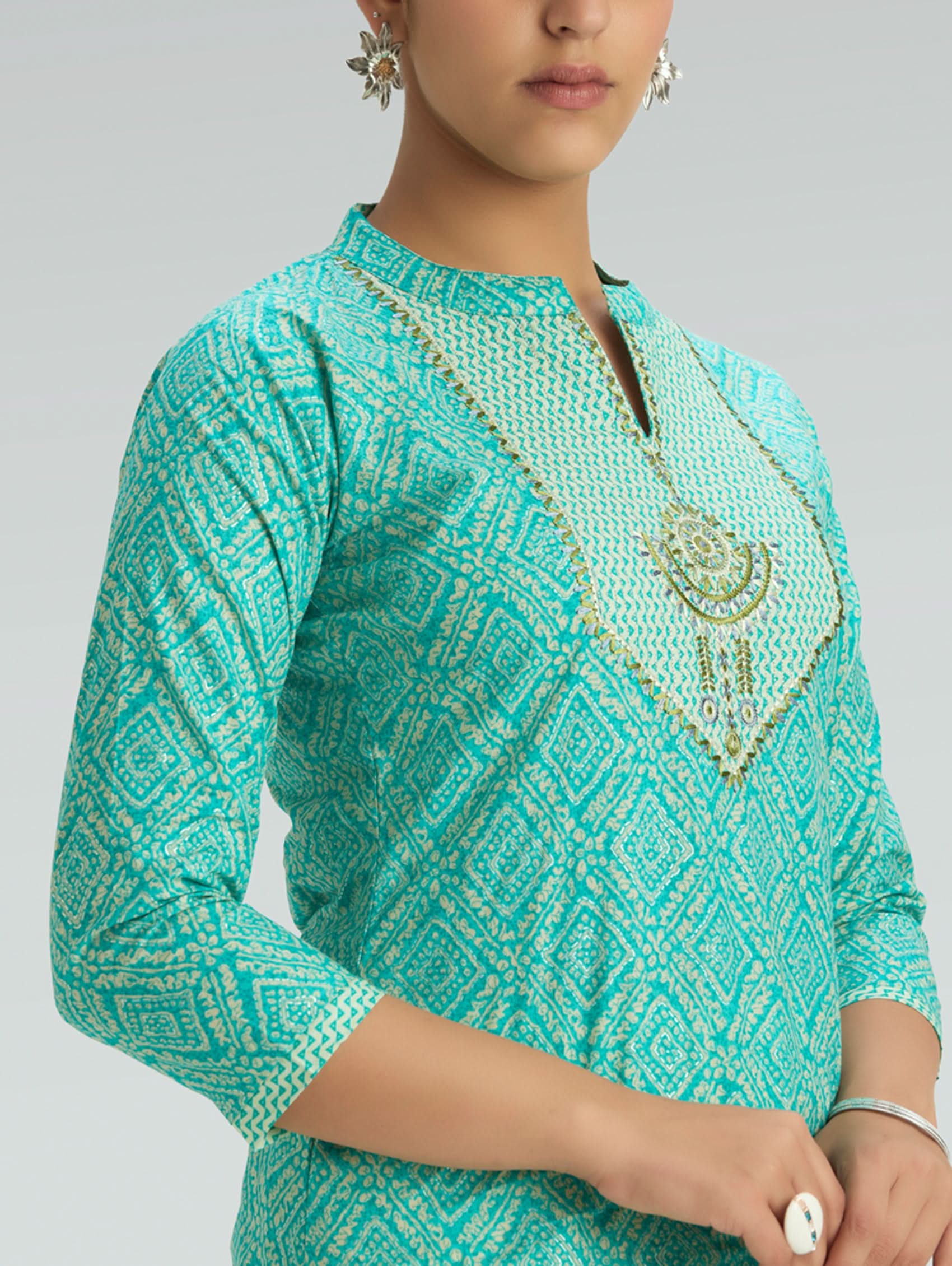 Teal patterned top worn by a person on a gray background