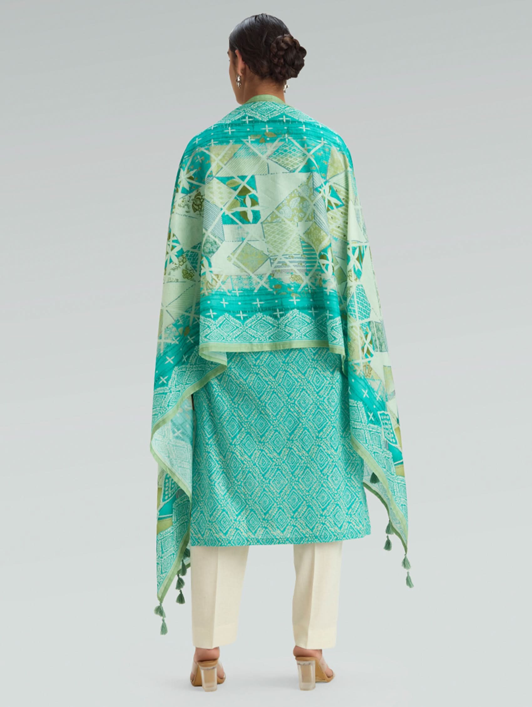 Person wearing a green patterned outfit with a matching shawl on a gray background