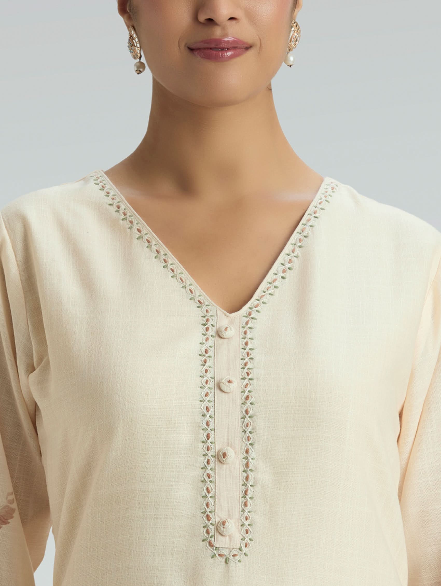 Close-up of a beige kurta with intricate detailing on a plain background