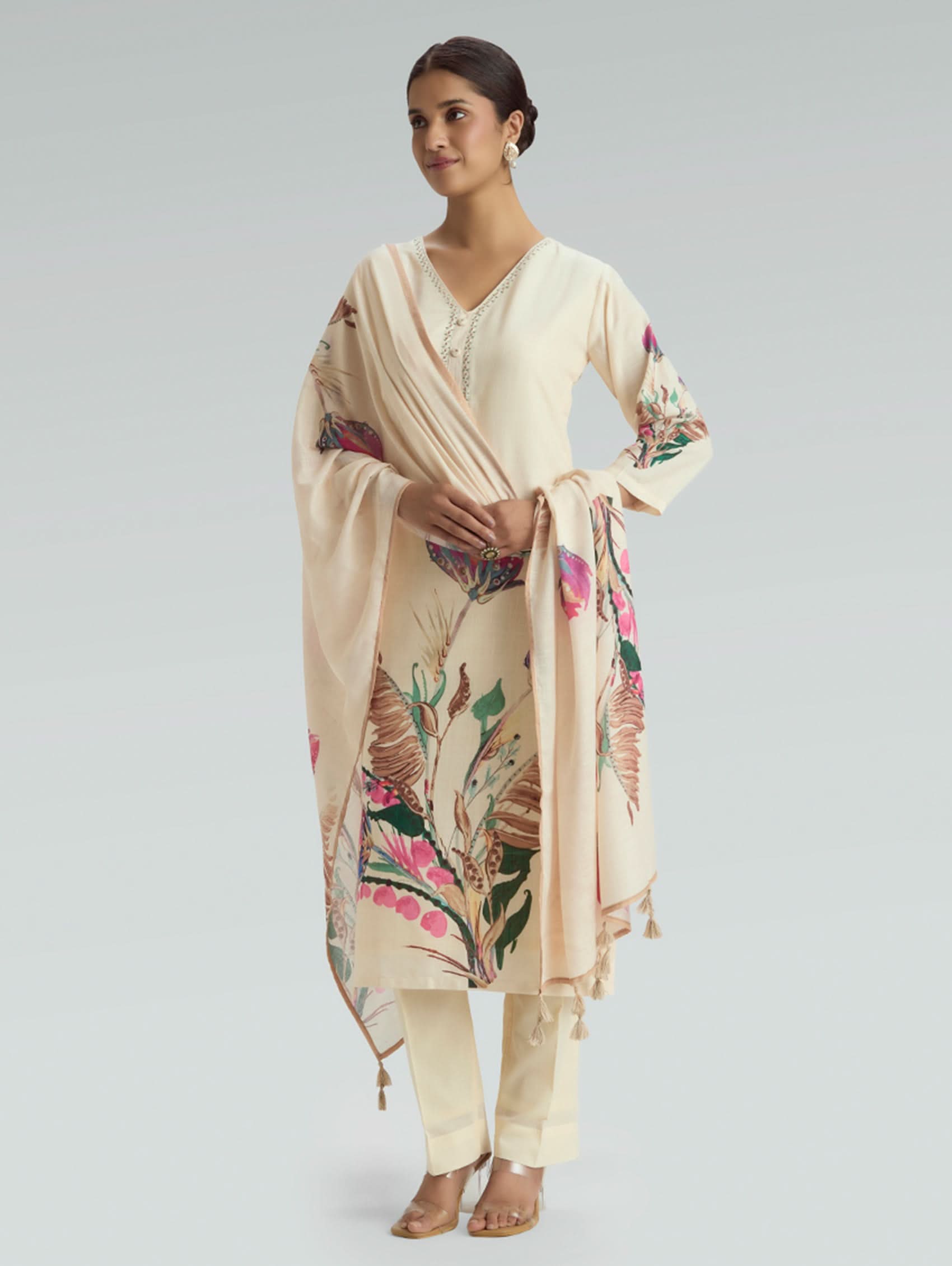 Woman wearing a beige outfit with floral patterns on a plain background
