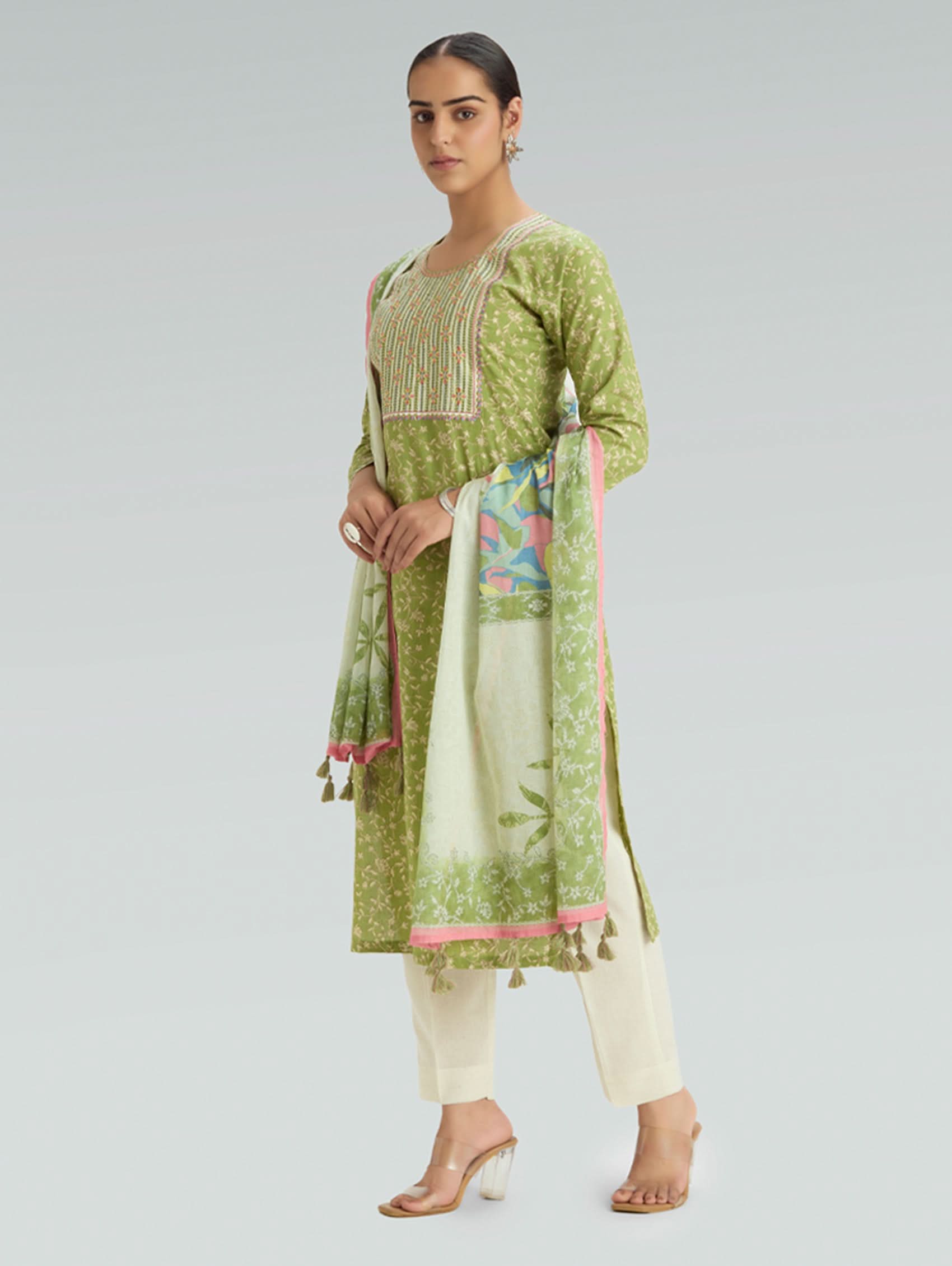 Woman wearing a green and white traditional outfit with a floral dupatta on a gray background