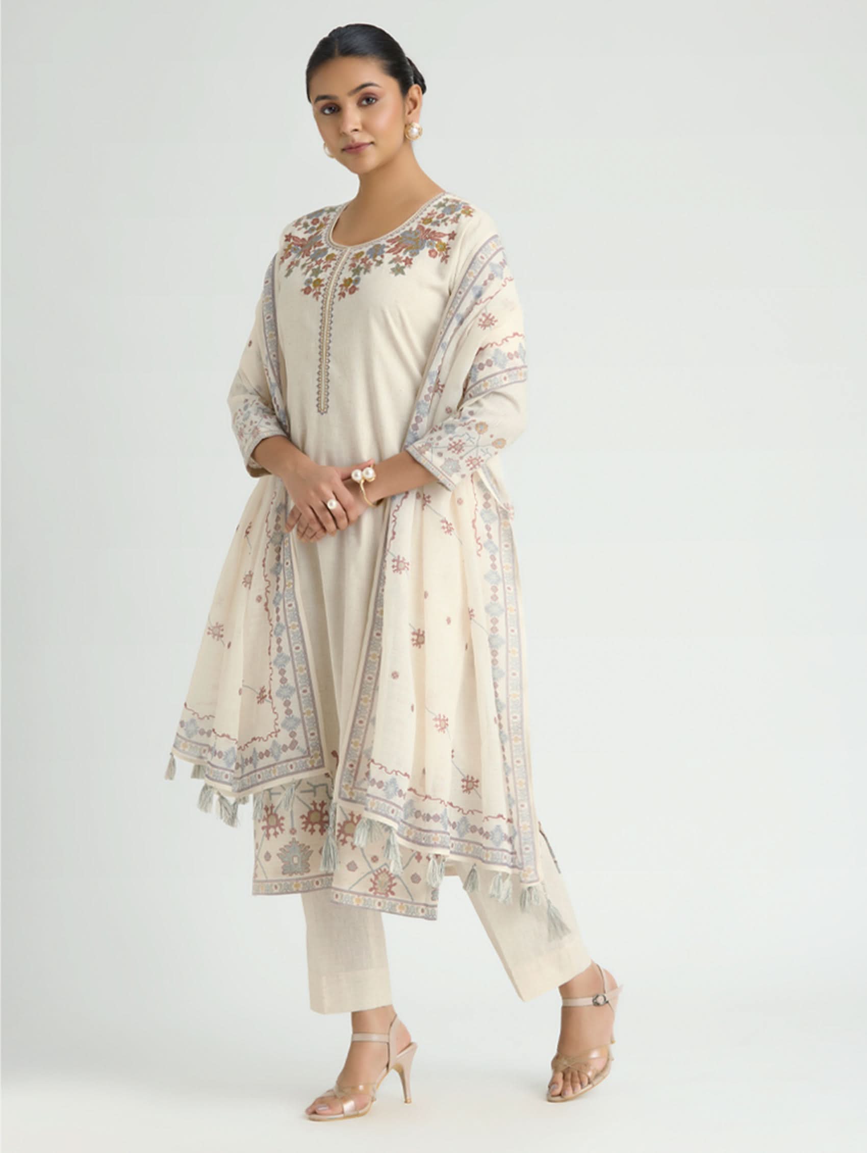 Woman wearing a cream-colored embroidered traditional outfit on a white background