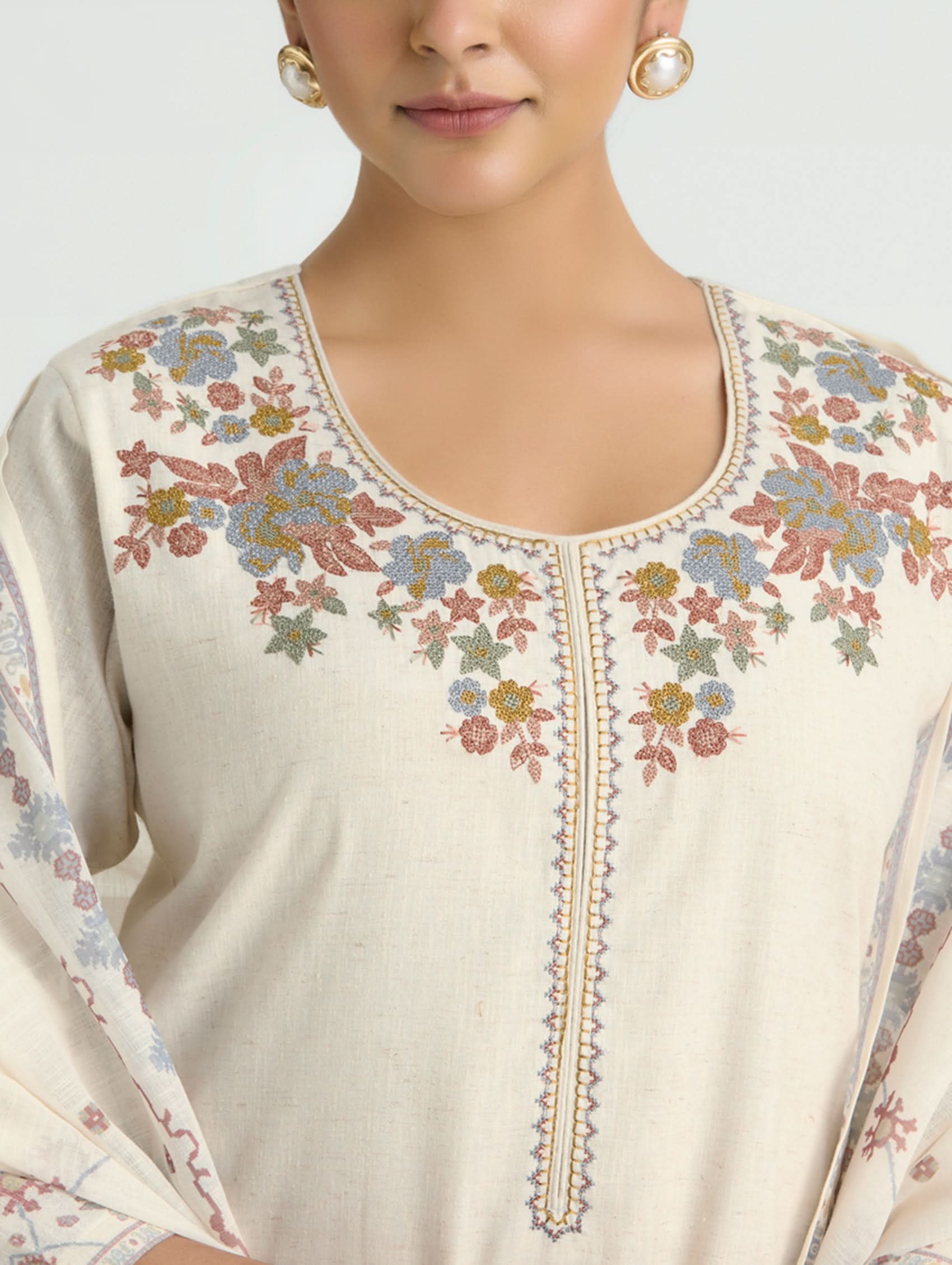 Close-up of a cream-colored embroidered top with floral patterns on a light gray background