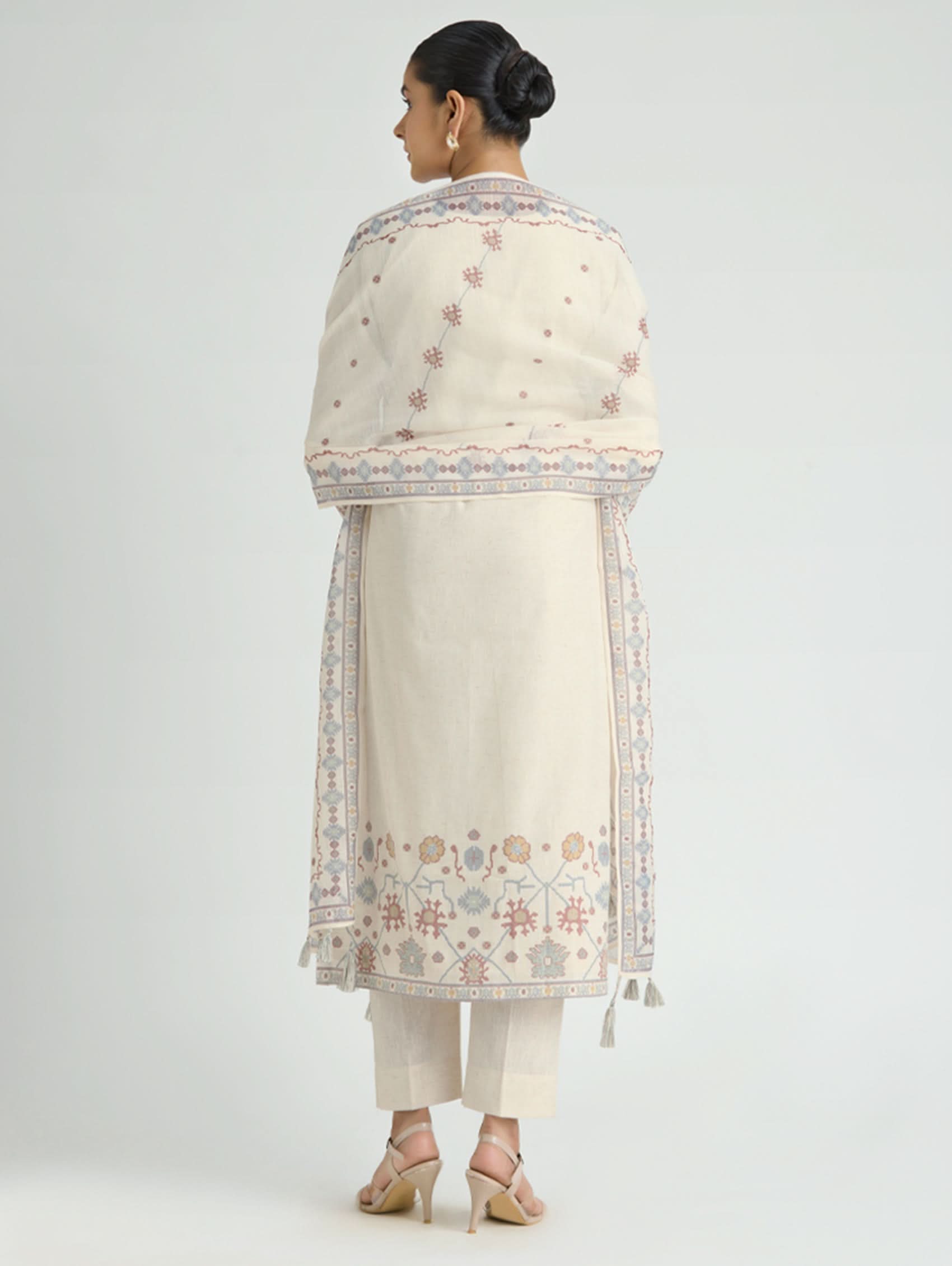 Woman wearing a cream embroidered traditional outfit on a white background