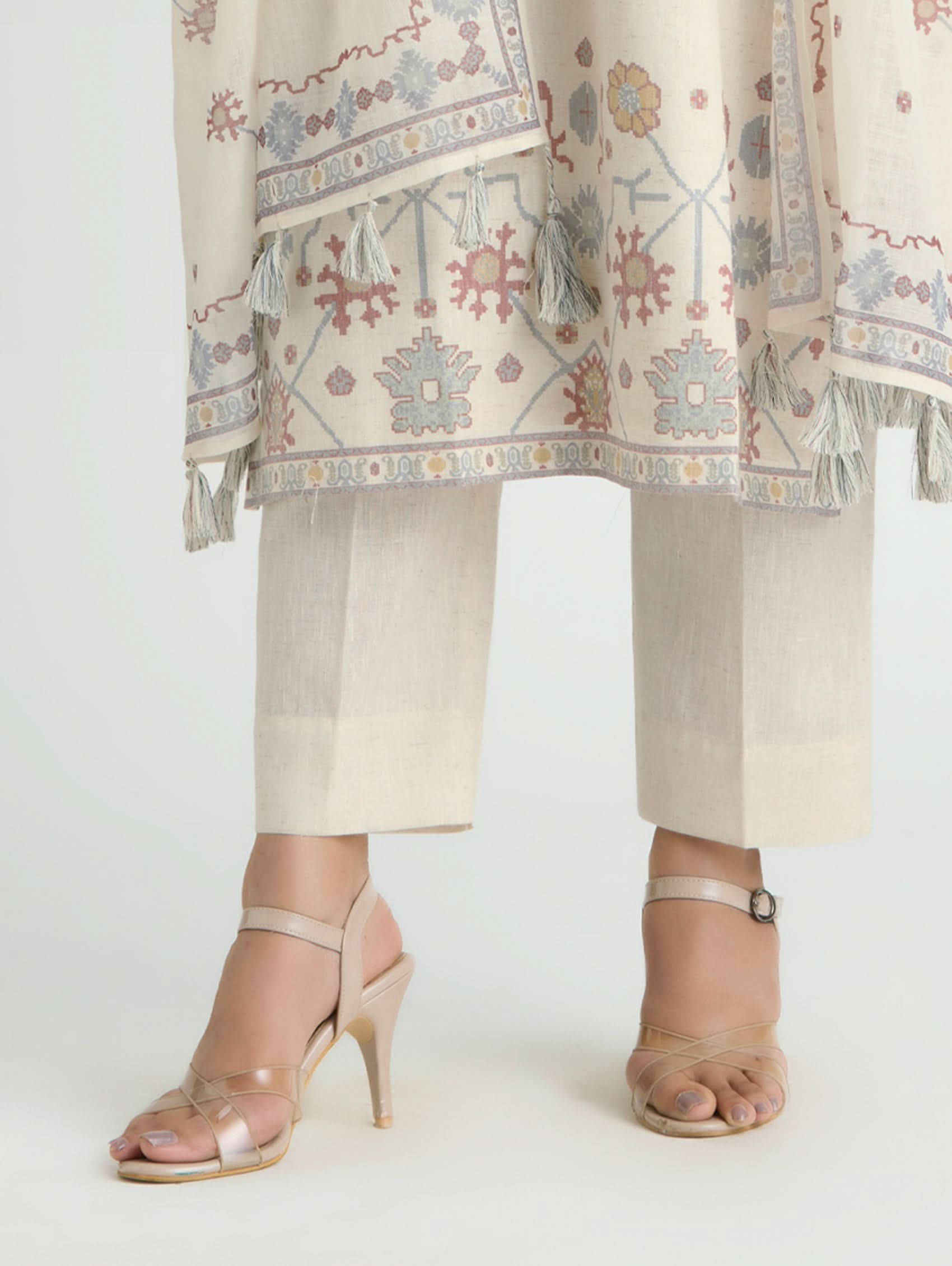 Person wearing a traditional outfit with a patterned shawl and beige pants on a white background