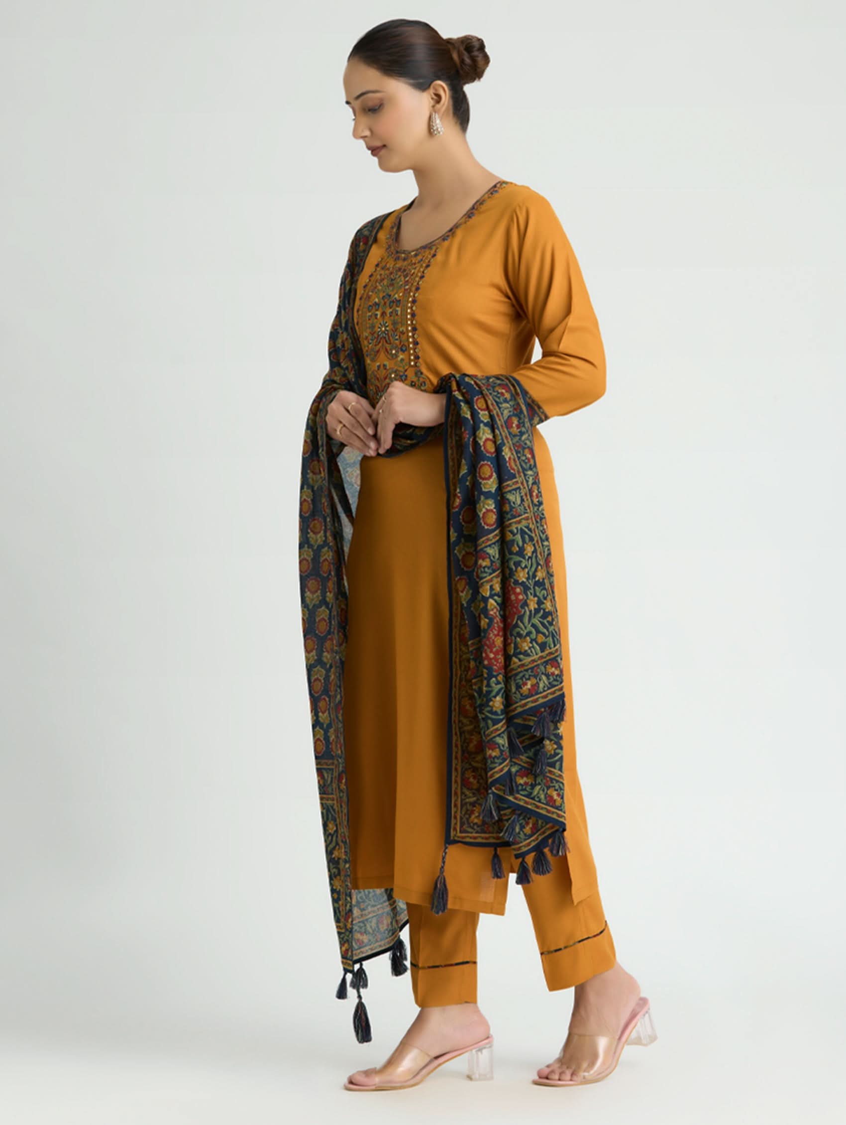 Woman wearing a mustard yellow traditional outfit with a patterned scarf on a white background