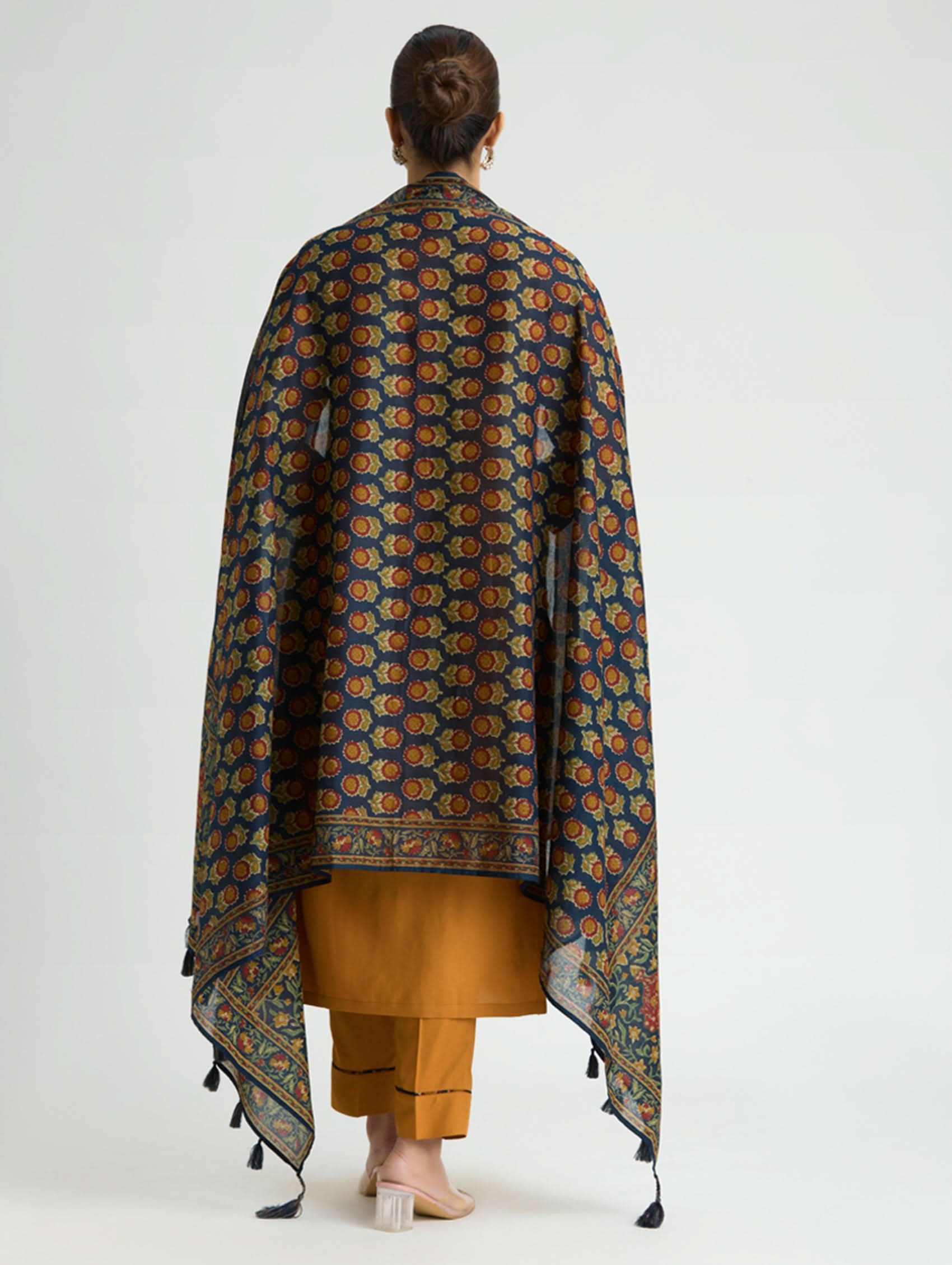 Woman wearing a patterned shawl over a mustard yellow outfit on a white background